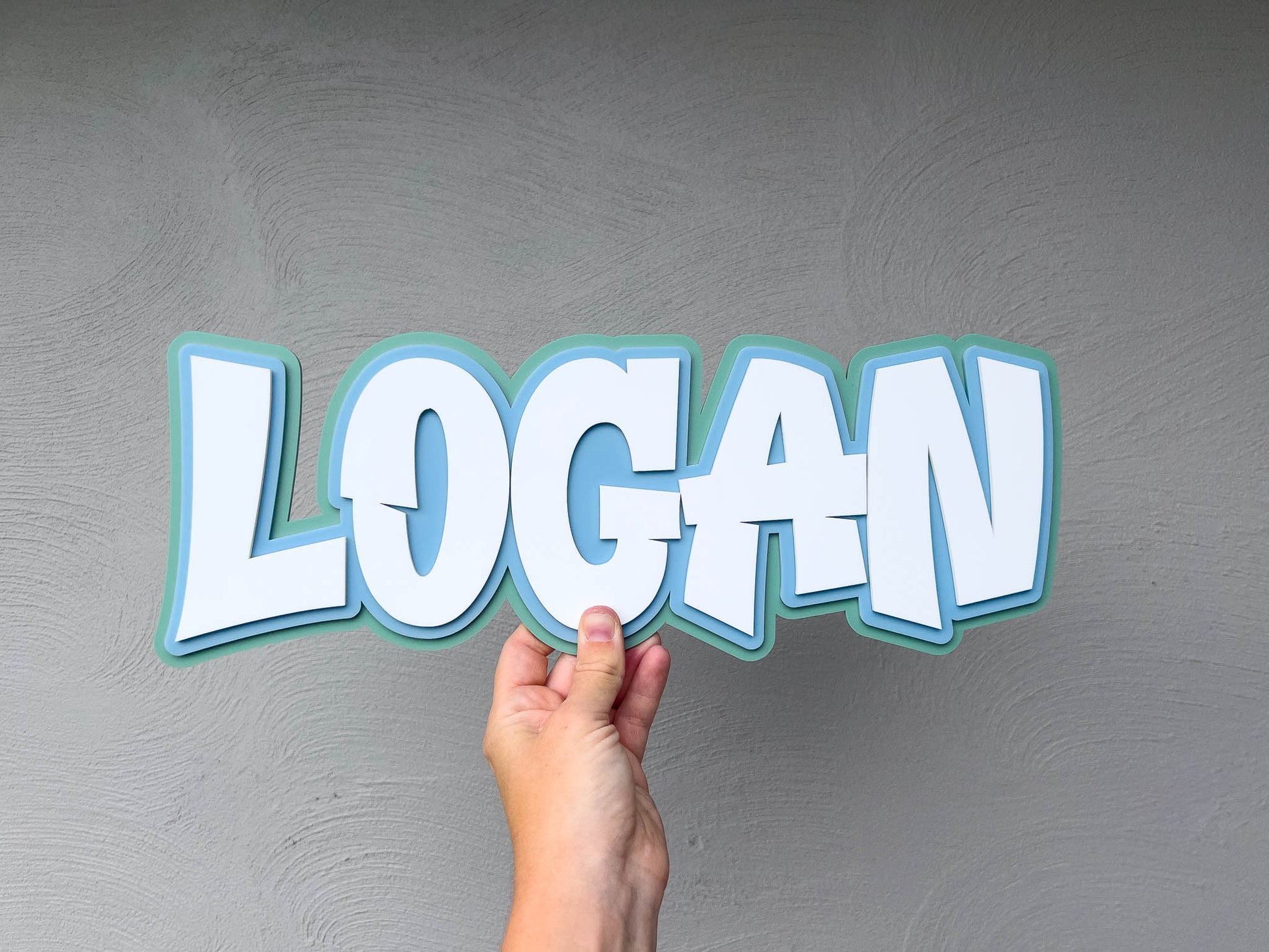 Personalised child's name plaque with 'LOGAN' in light blue, light green and white.