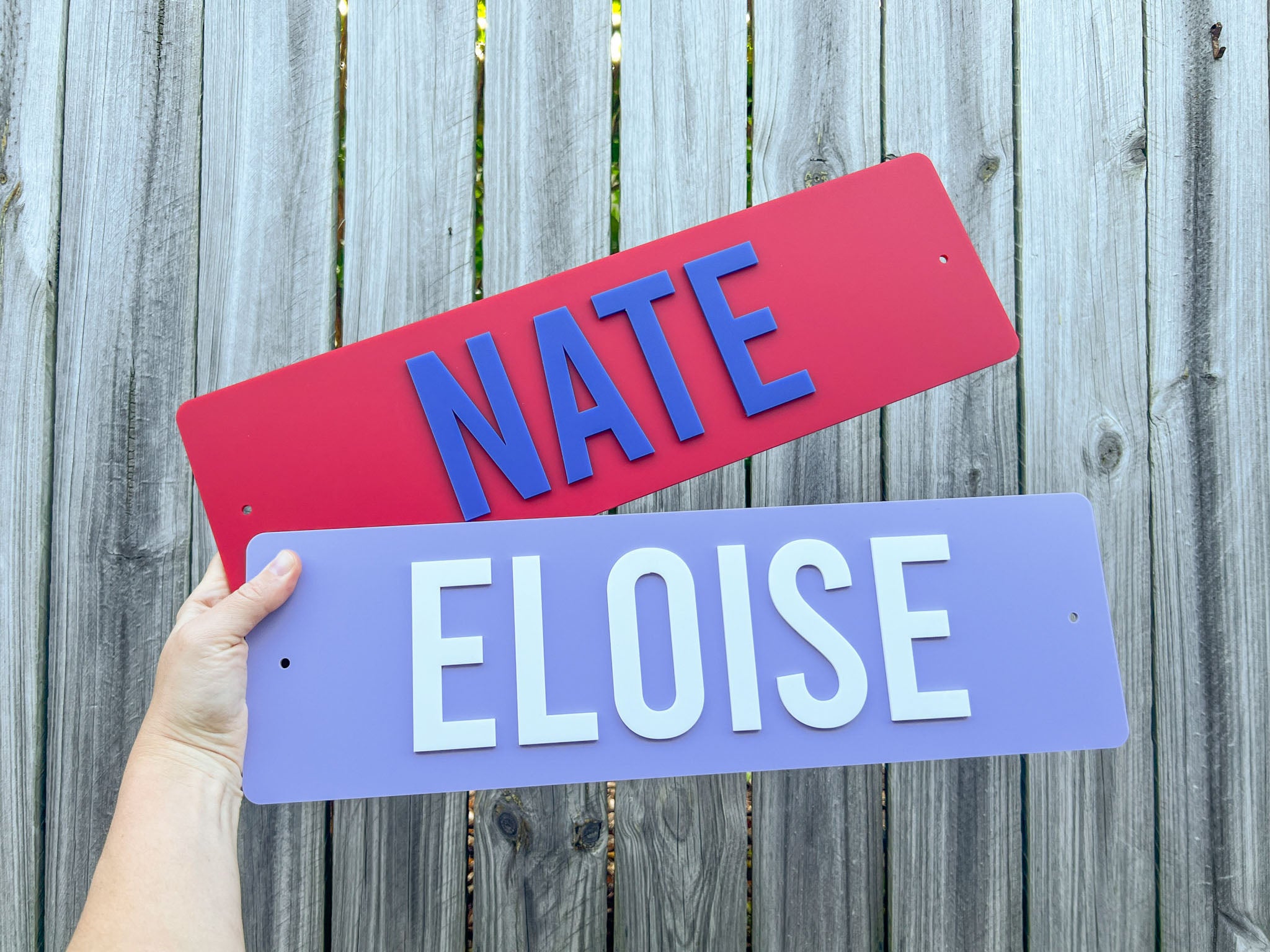 Two custom laser cut acrylic name plaques with the names 'NATE' & 'ELOISE' in red and purple.