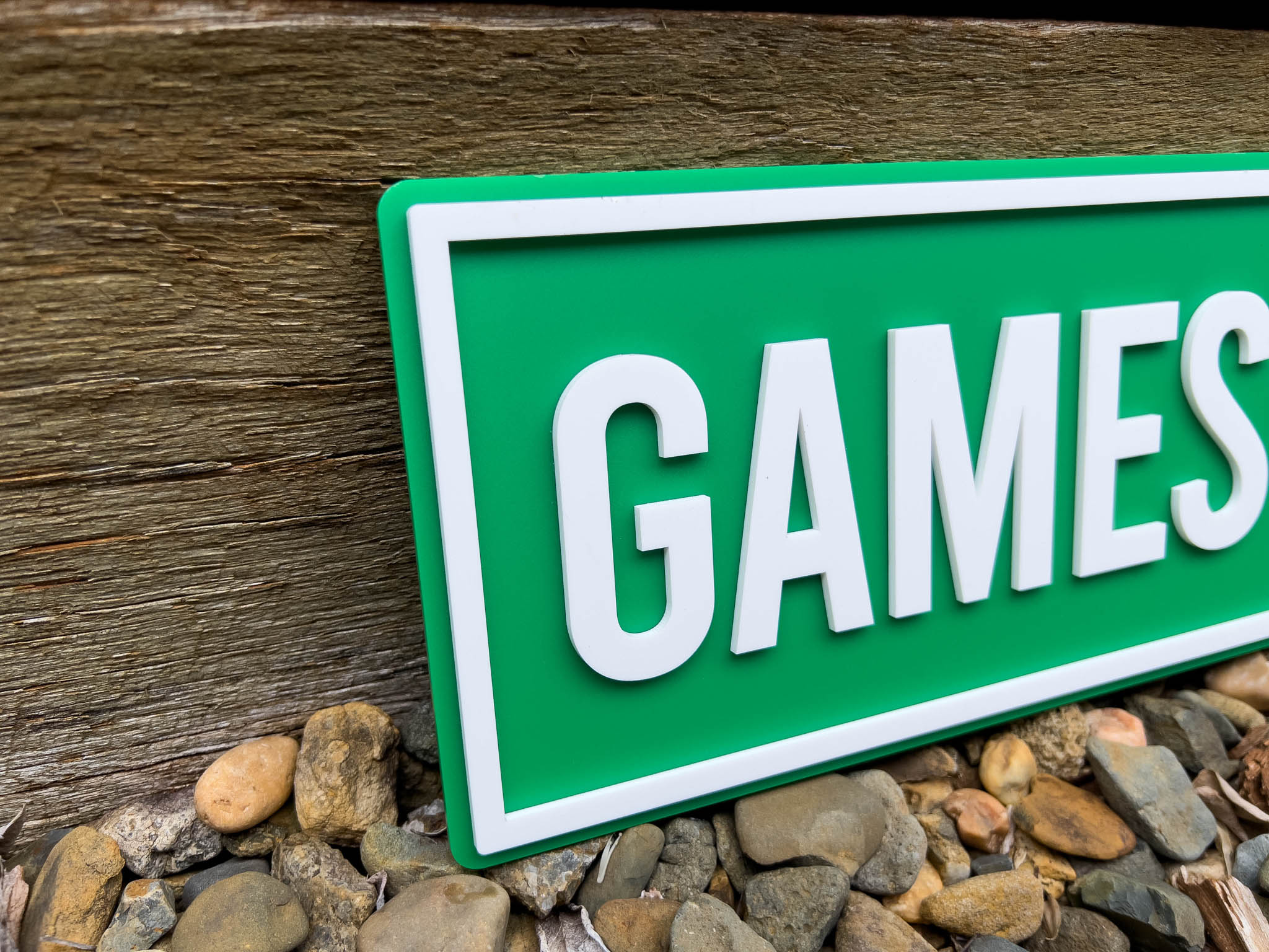 Green sign with 'GAMES' text on a wooden surface with stones | Coji Designs