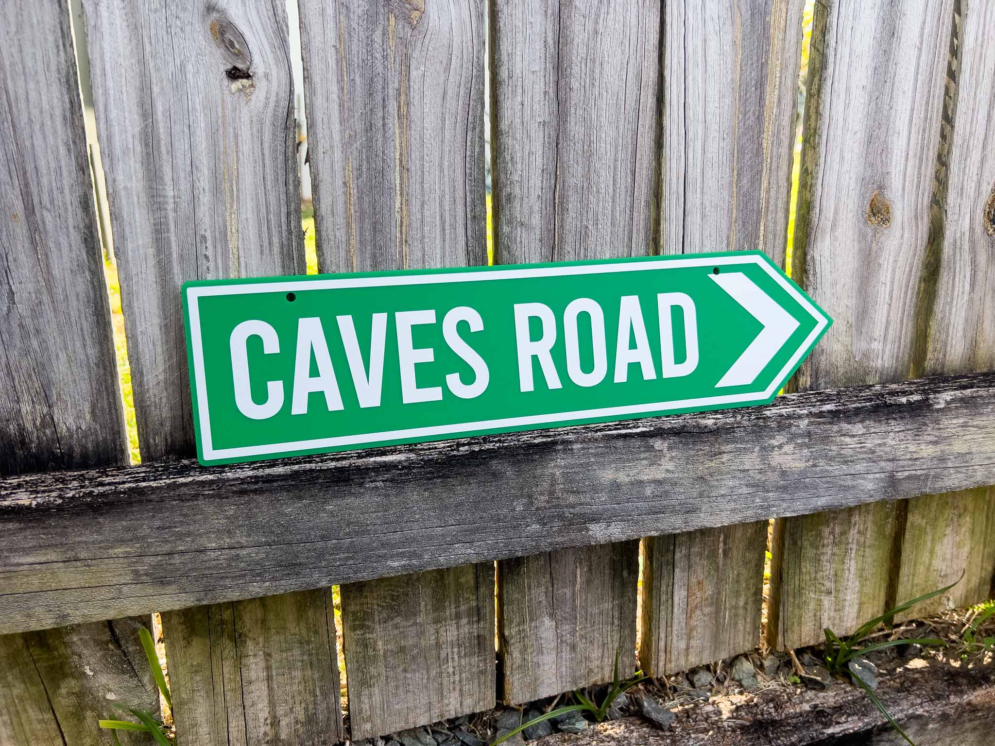 Custom printed green sign with 'CAVES ROAD' text on a wooden fence background