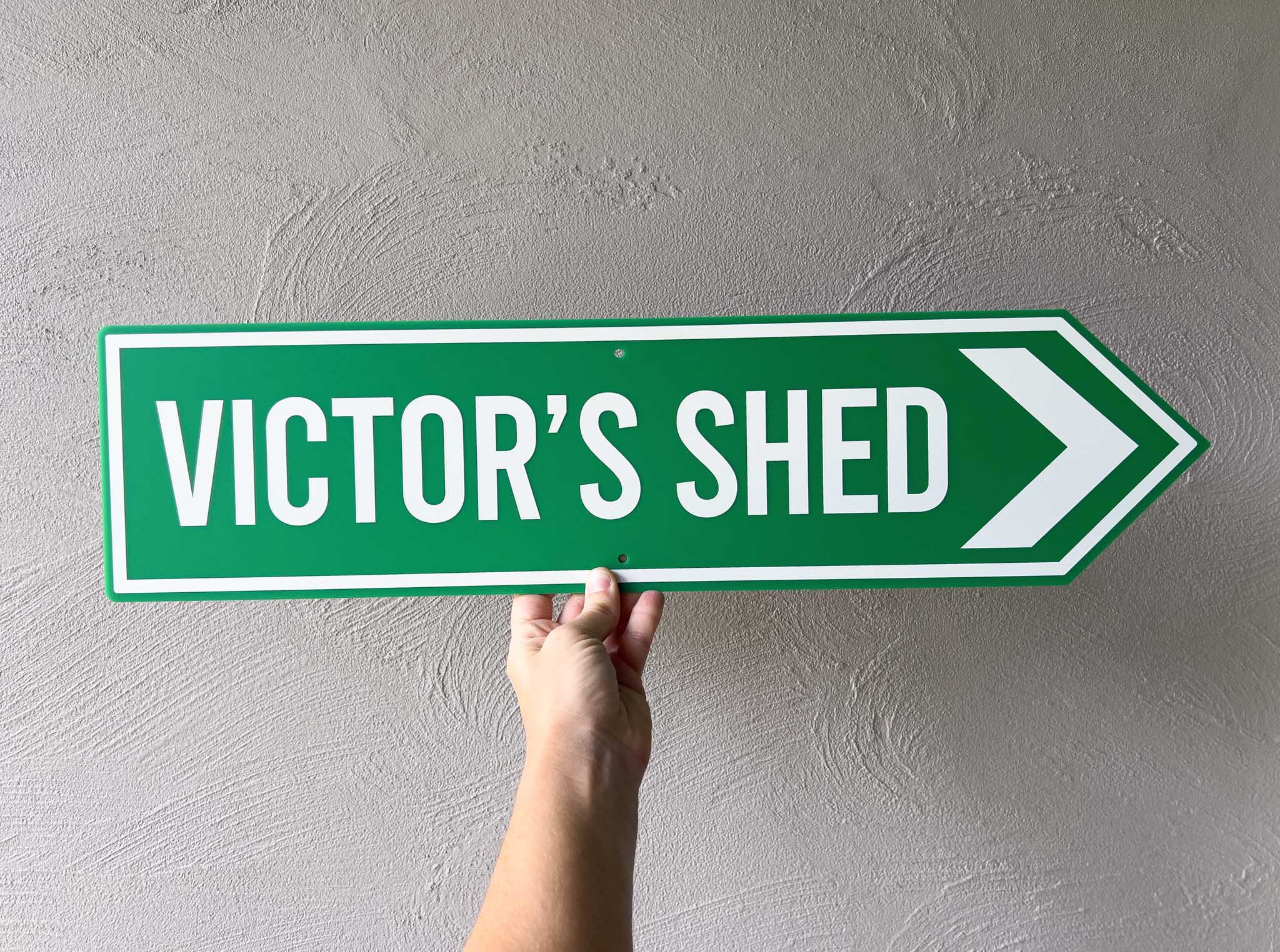 Iconic retro highway pointer sign with 'Victor's Shed' text against a grey wall