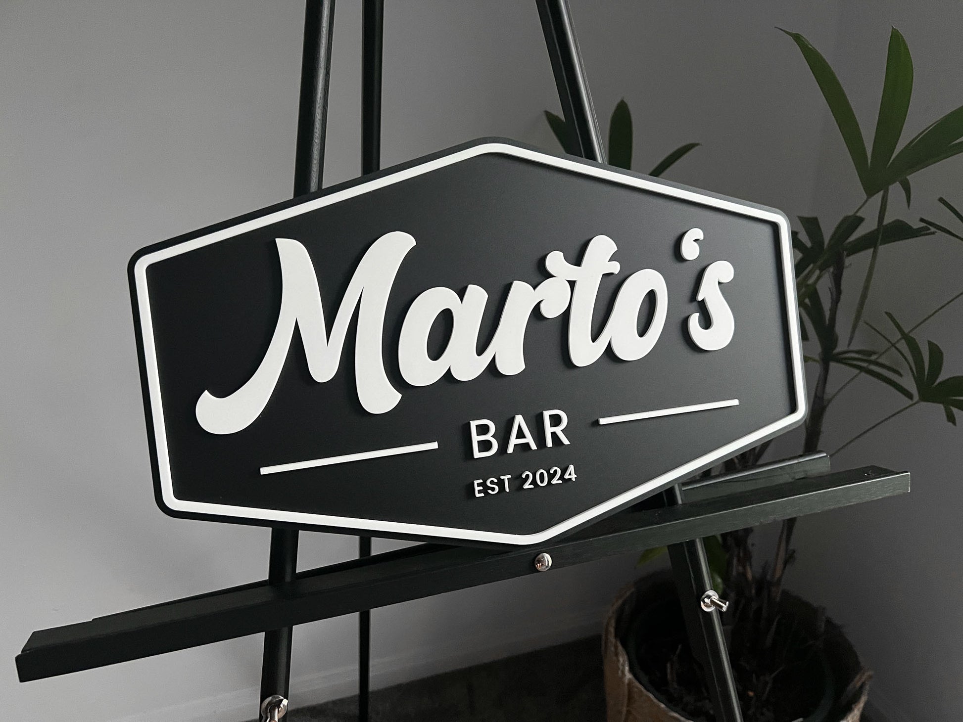 Black and white personalsied sign with 'Marto's Bar' on a stand against a grey background.
