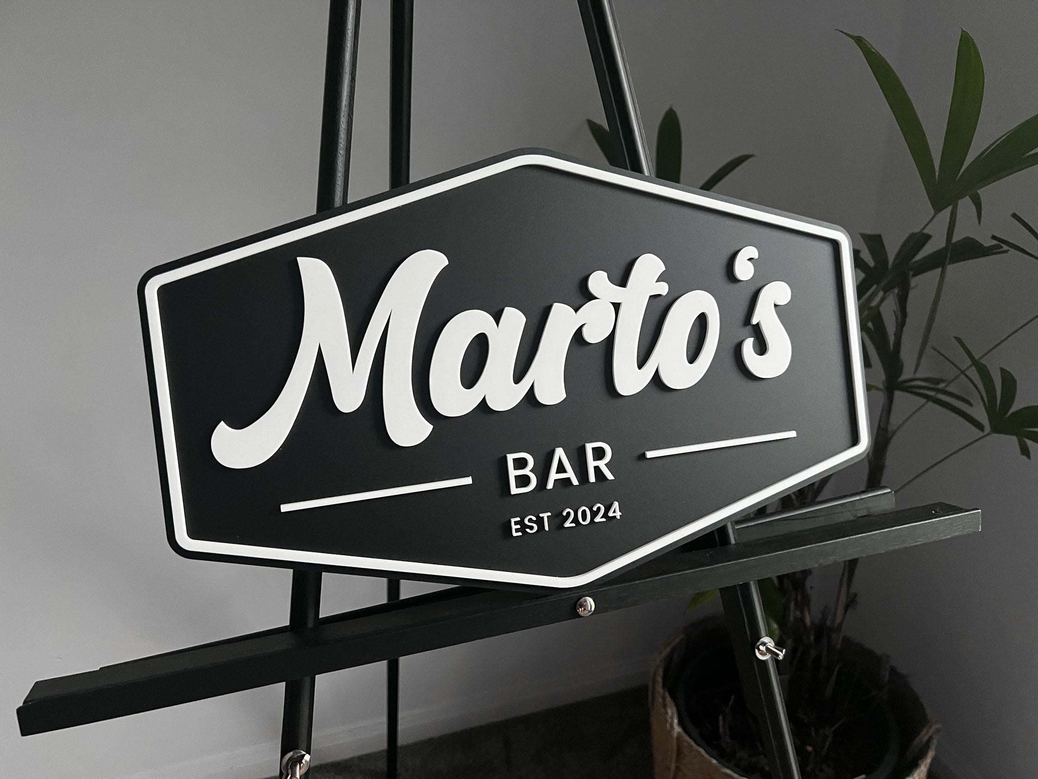 Black and white personalsied sign with 'Marto's Bar' on a stand against a grey background.