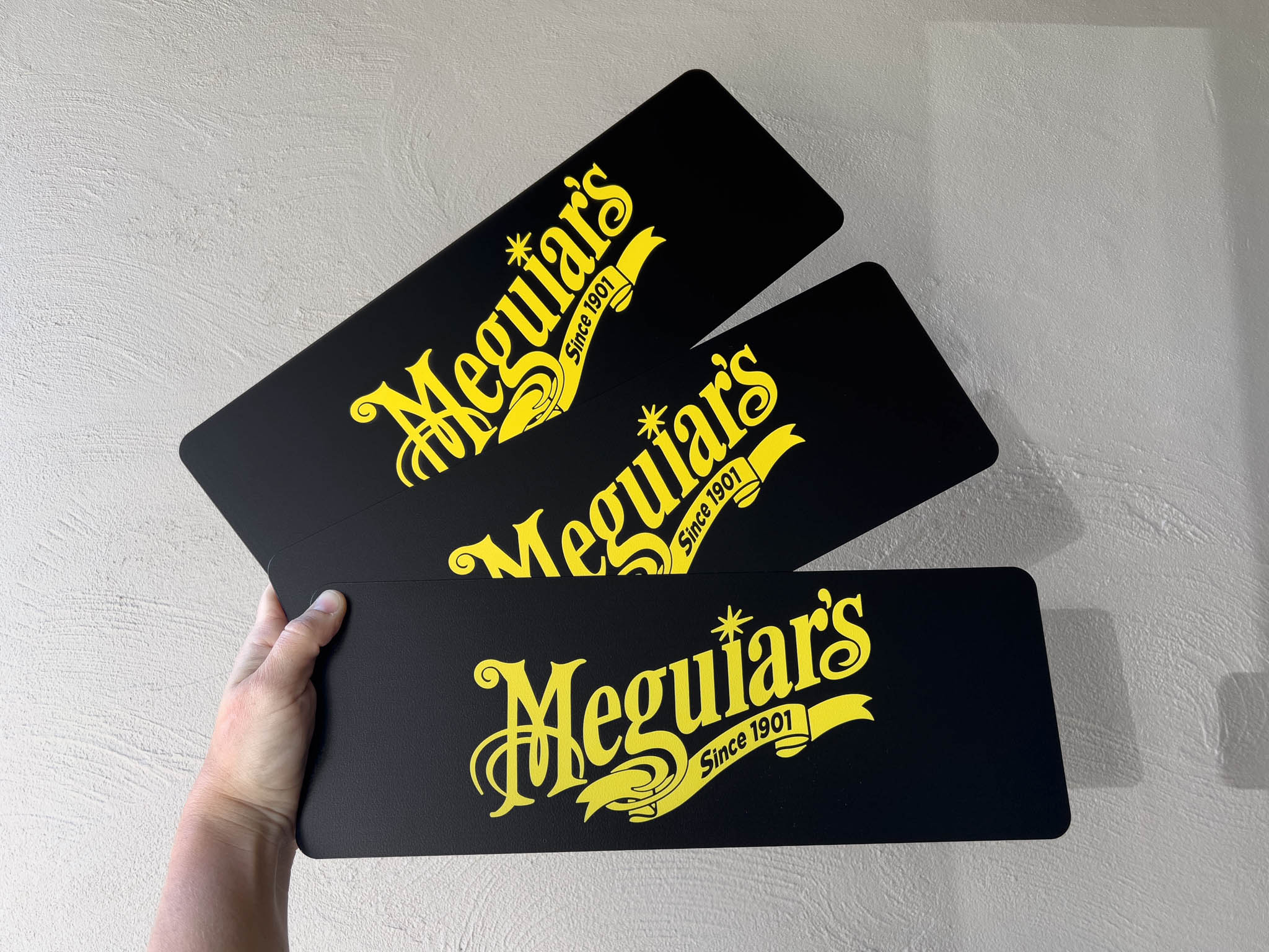 Three black custom printed aluminium logo plates with yellow 'Meguiar's' logo on a black background.