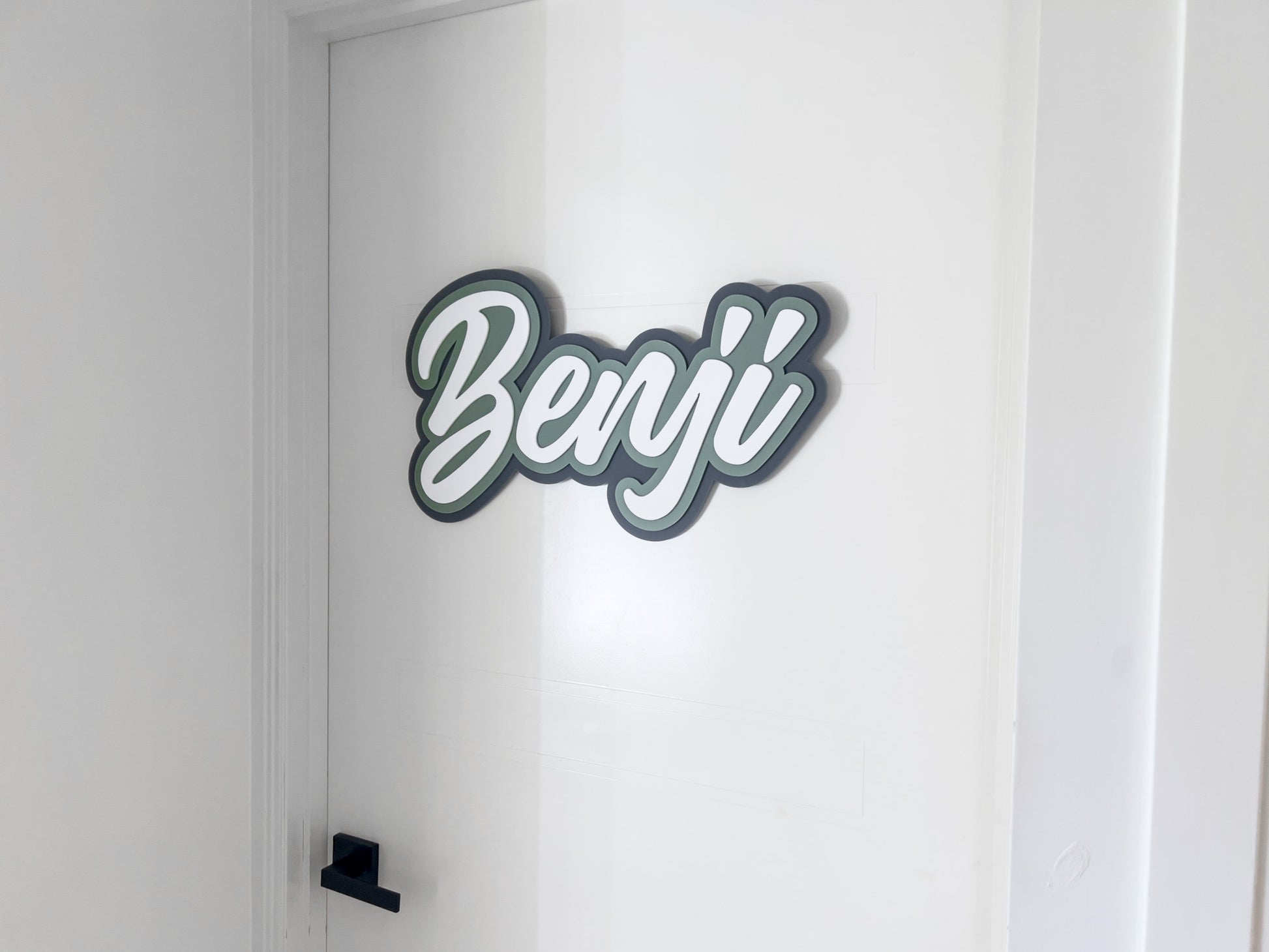 Custom 3D acrylic door plaque that reads 'Benji' laser cut in shades of green, grey and white.