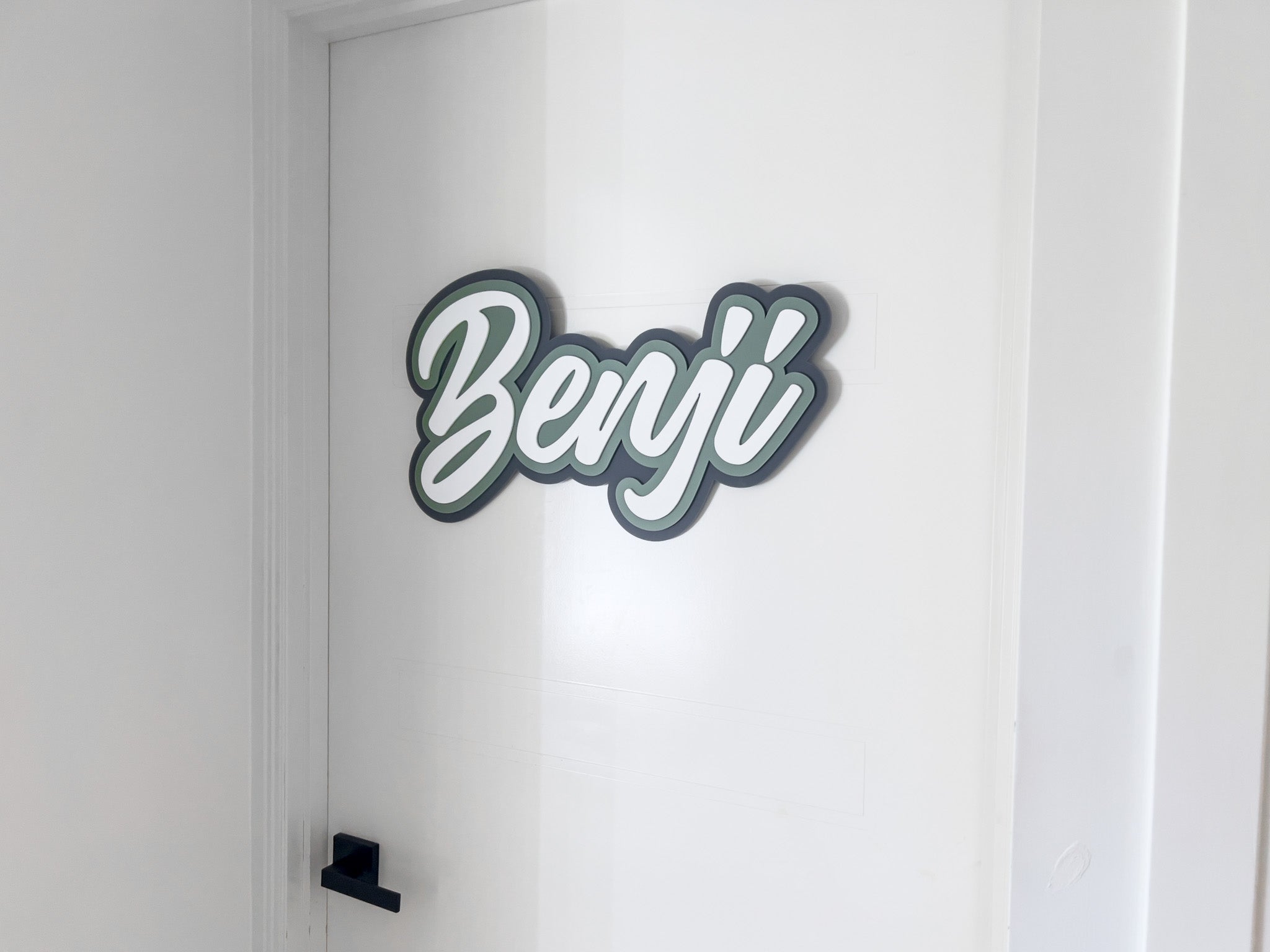 Custom 3D acrylic door plaque that reads 'Benji' laser cut in shades of green, grey and white.