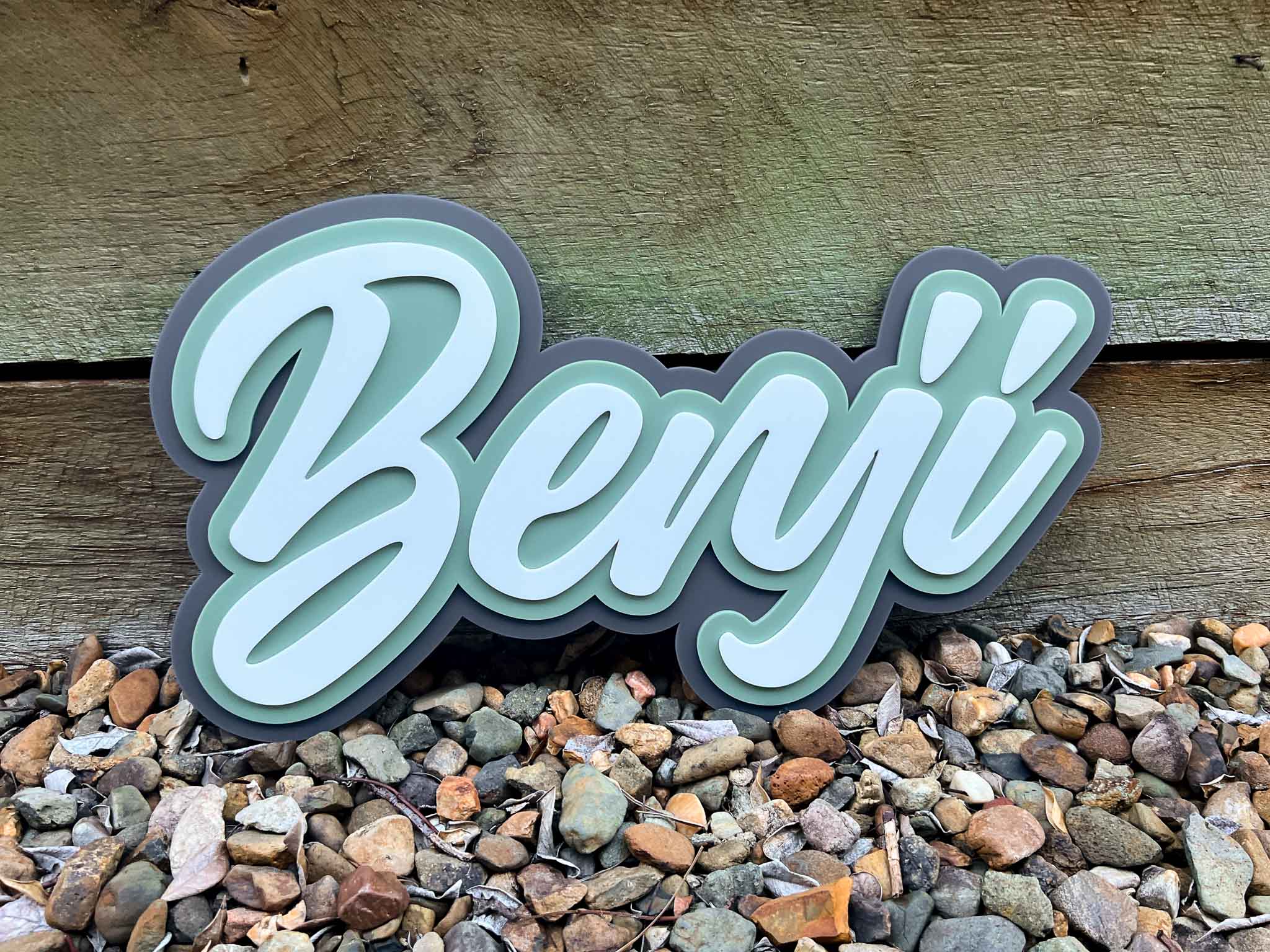 Decorative name sign 'Benji' on a wooden background with pebbles