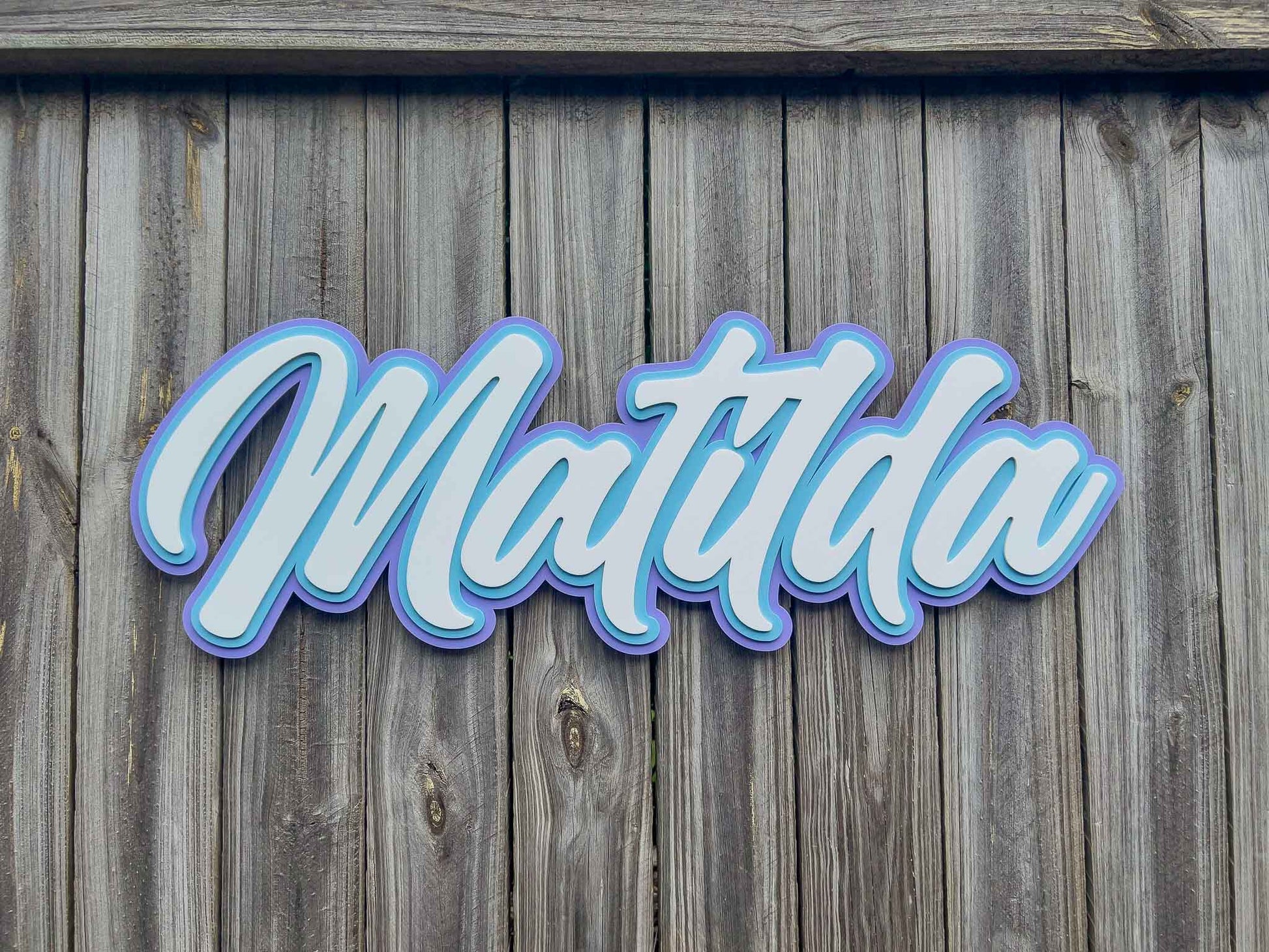 A surf typography style name plaque that says 'Matilda' that has been custom cut in purple, light blue and white acrylic.