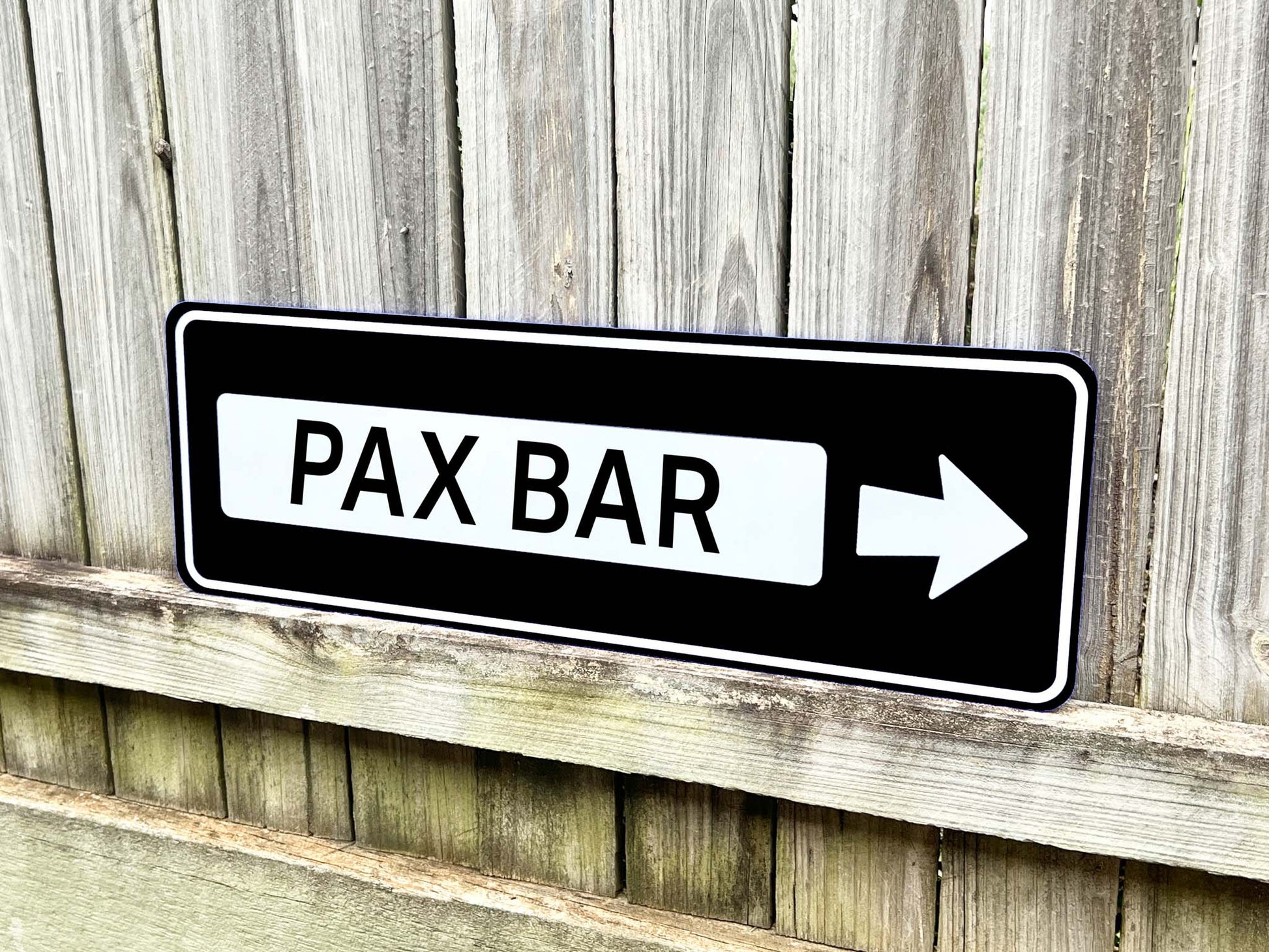 Classic highway style direction sign that reads 'PAX BAR' in black and white.