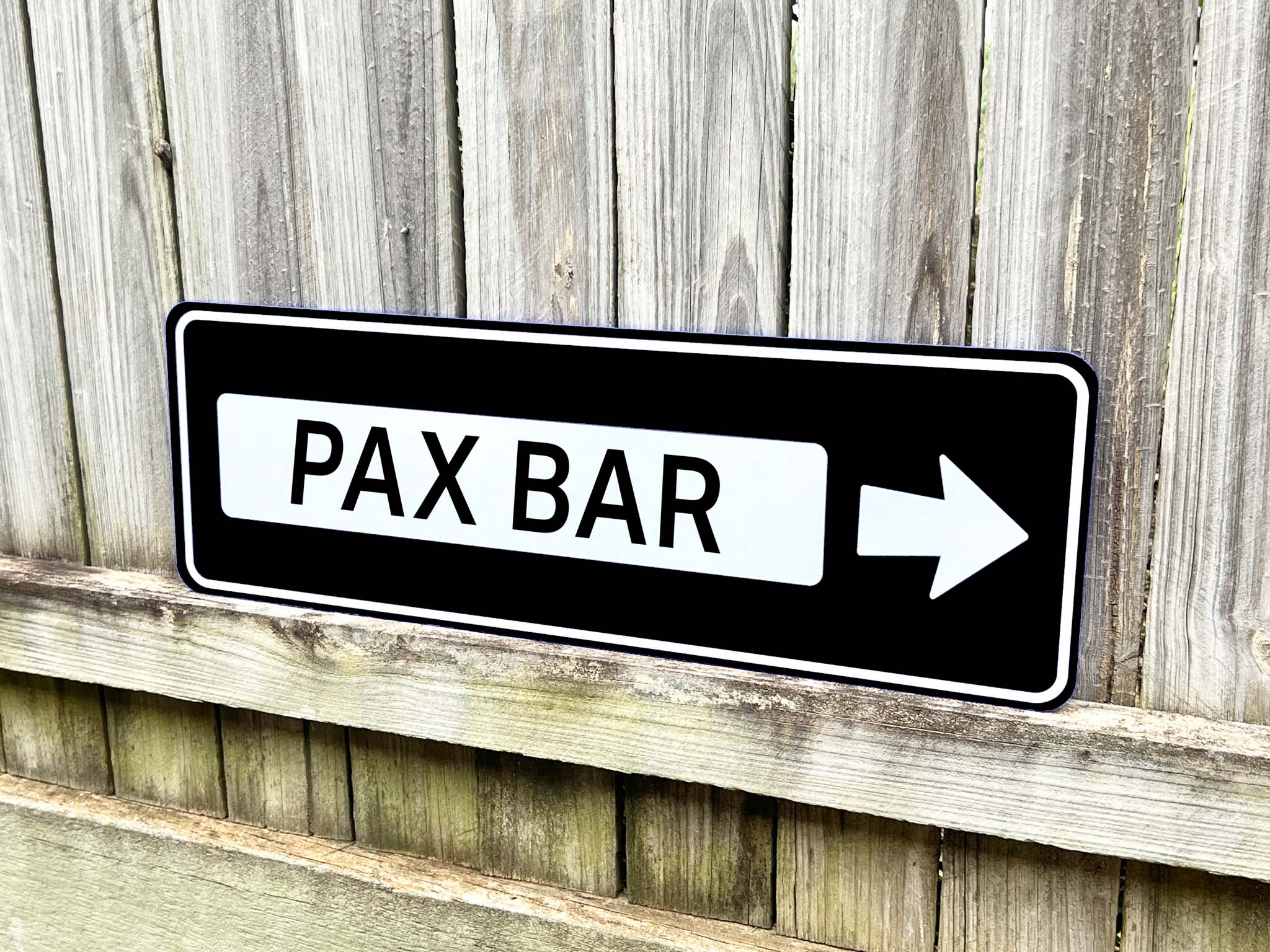 Classic highway style direction sign that reads 'PAX BAR' in black and white.