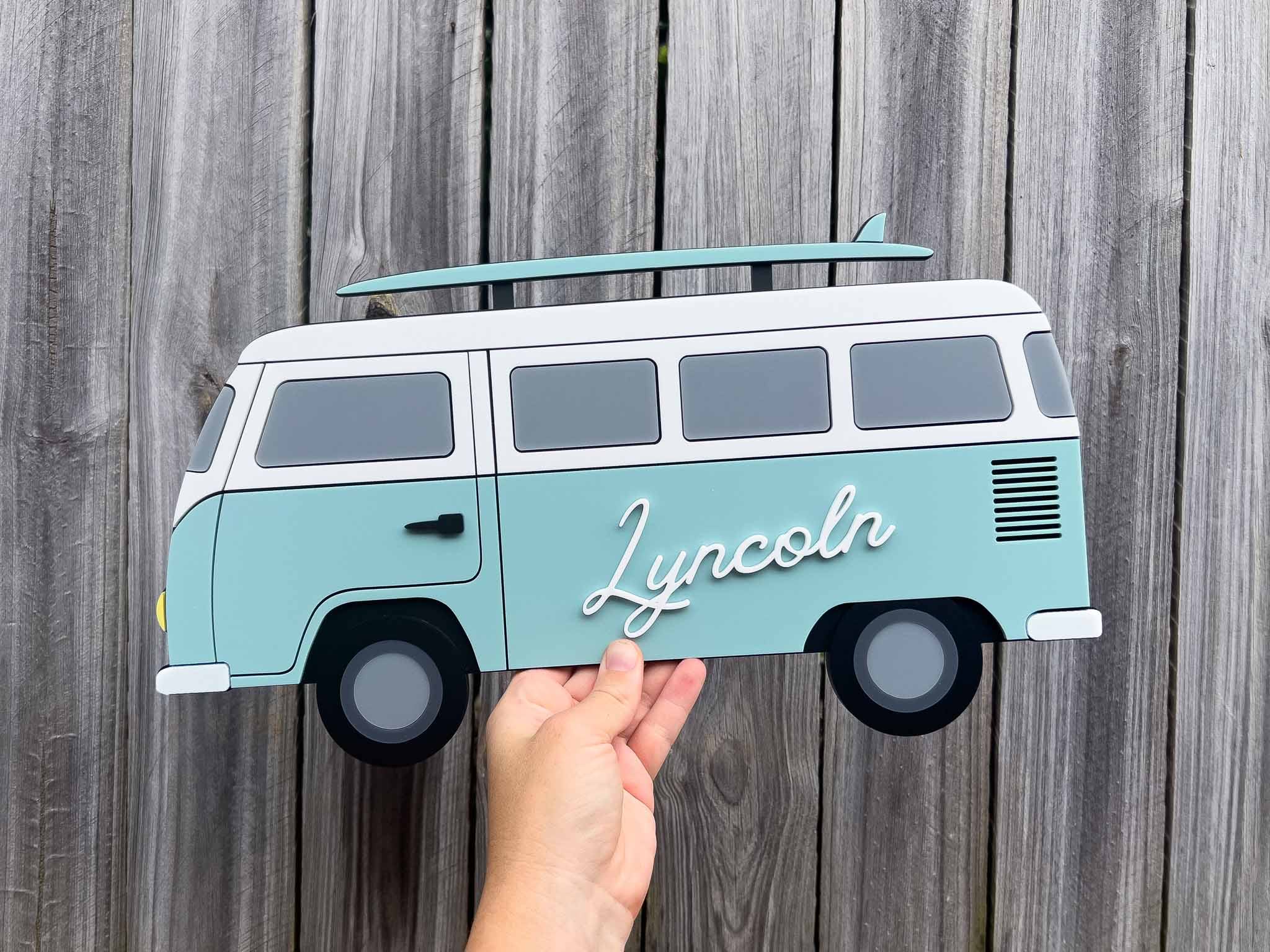 Seafoam green beach van-shaped sign with 'Lyncoln' on a wooden background