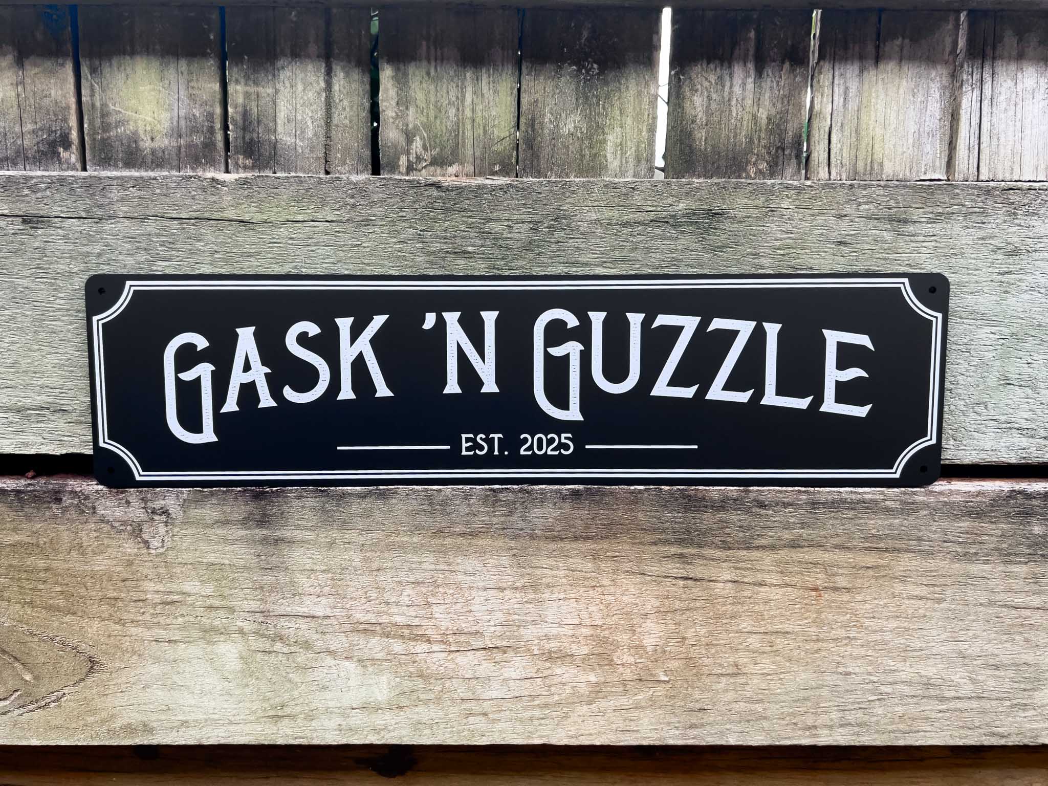 Decorative personalised bar sign with 'Gask 'N Guzzle' text on a wooden background