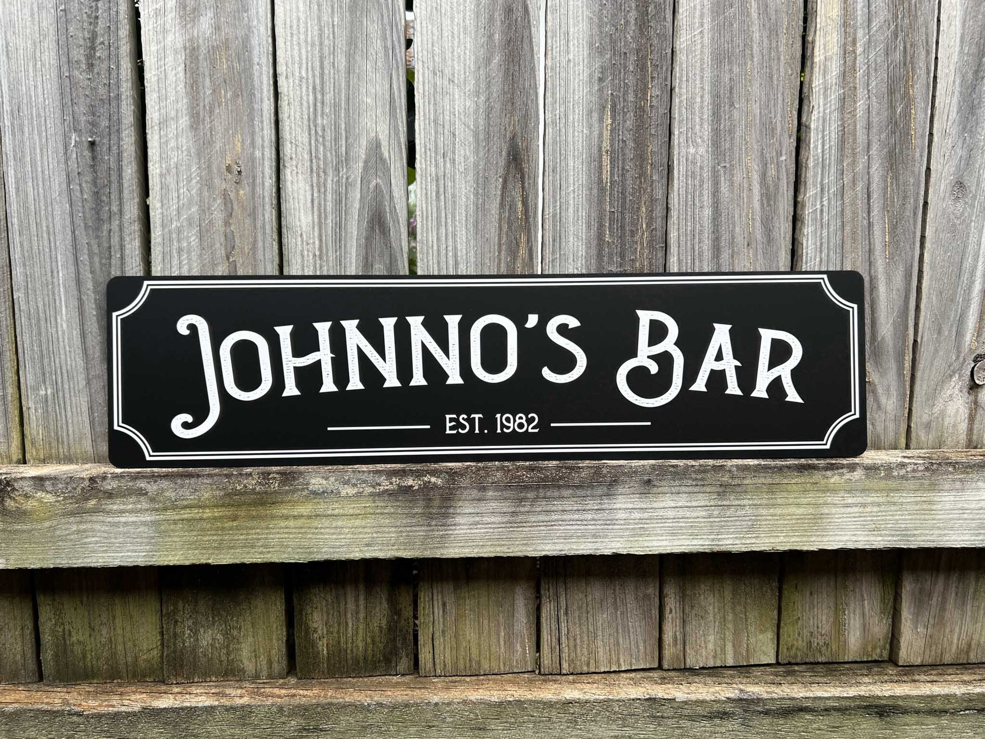 UV printed texture sign with 'JOHNNOS BAR EST. 1982' text against a wooden background
