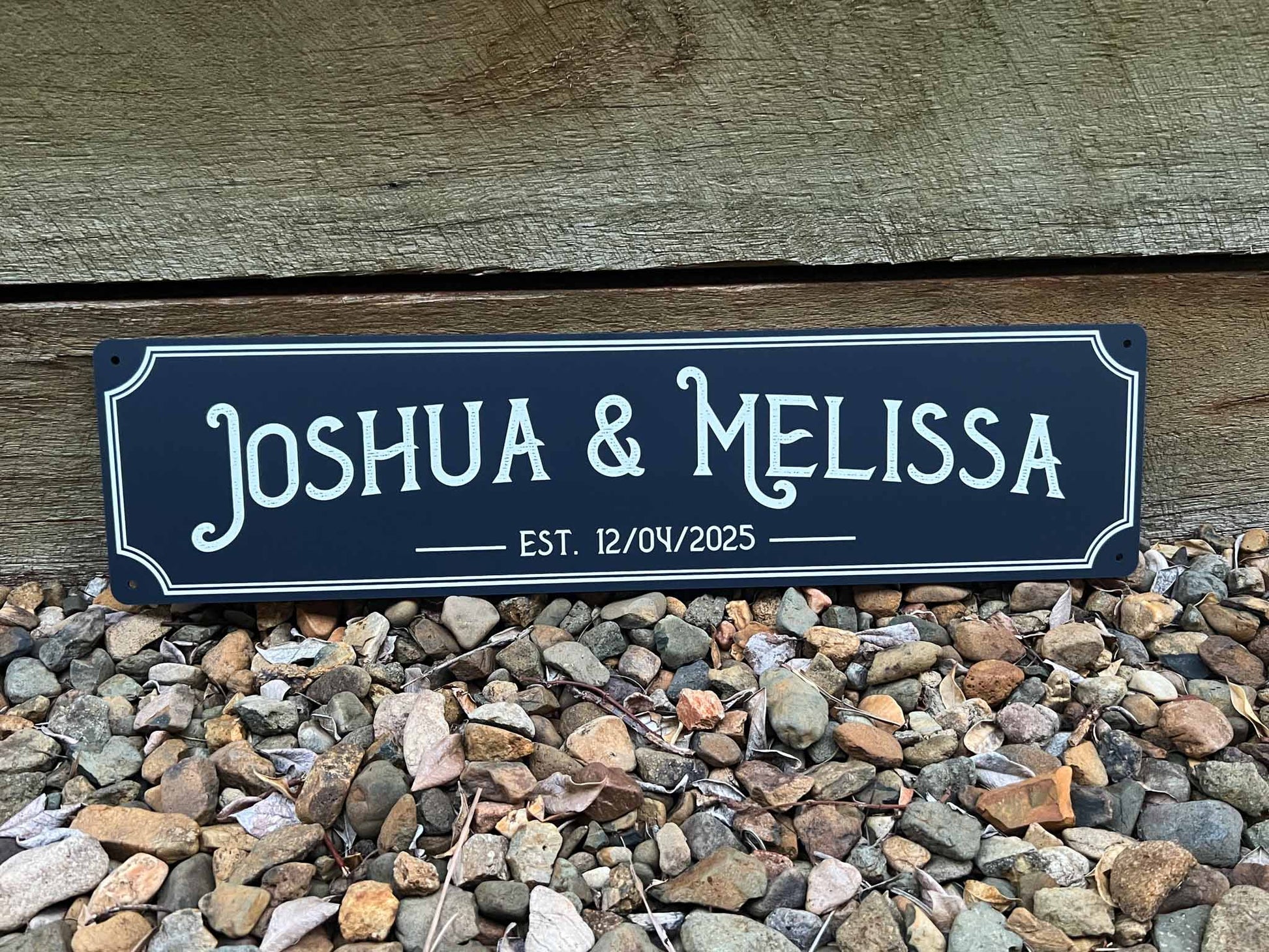 A deep sea blue coloured sign with white vintage text that says the names 'Joshua & Melissa'.