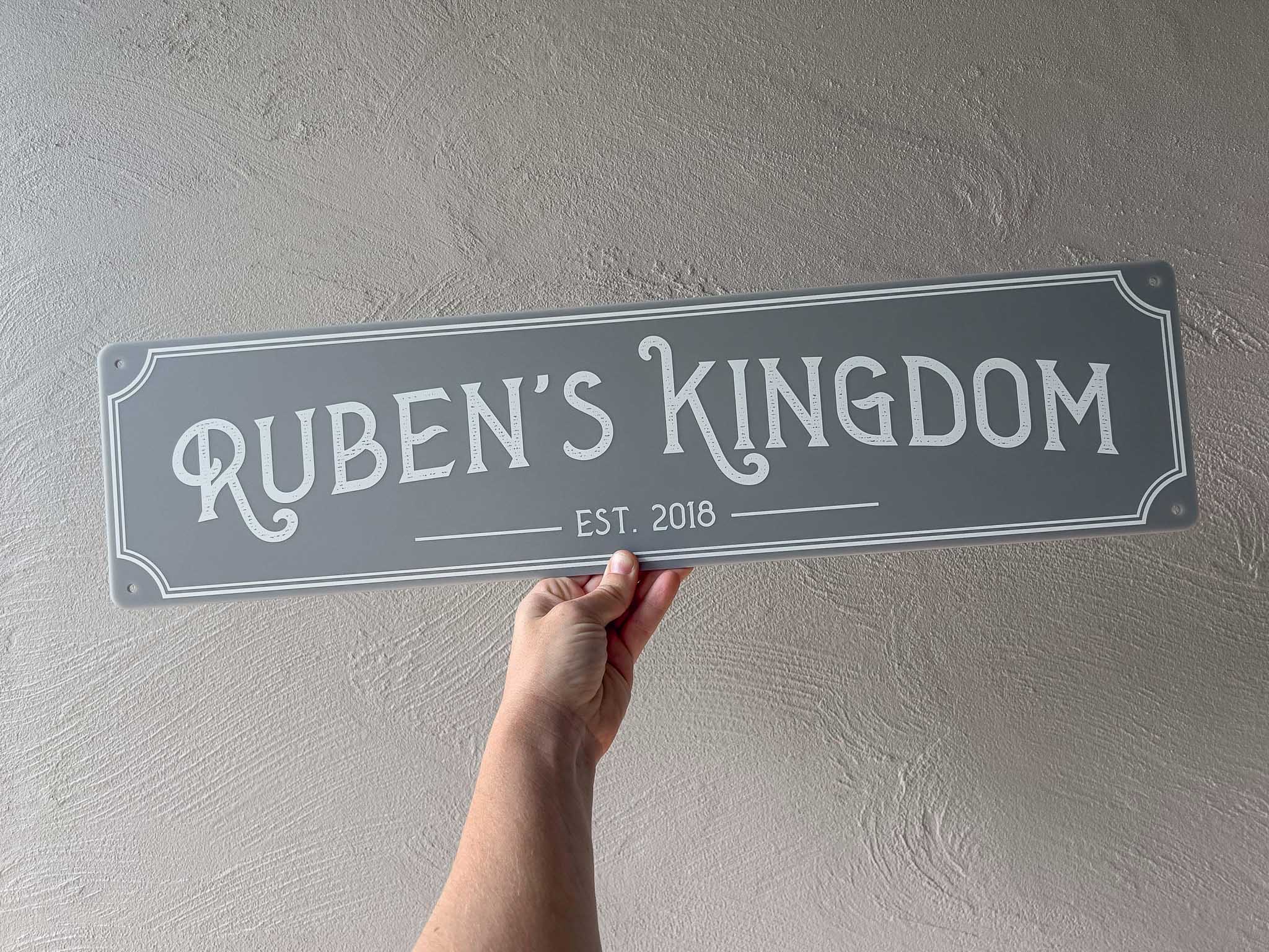 A light grey and white custom printed bar sign that says 'Ruben's Kingdom Est. 2018'.