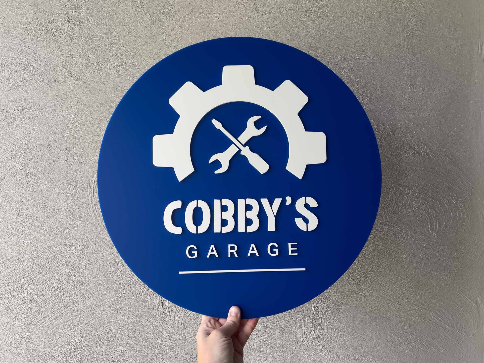 Personalised blue and white mechanic shop style sign that says 'Cobby's Garage'.