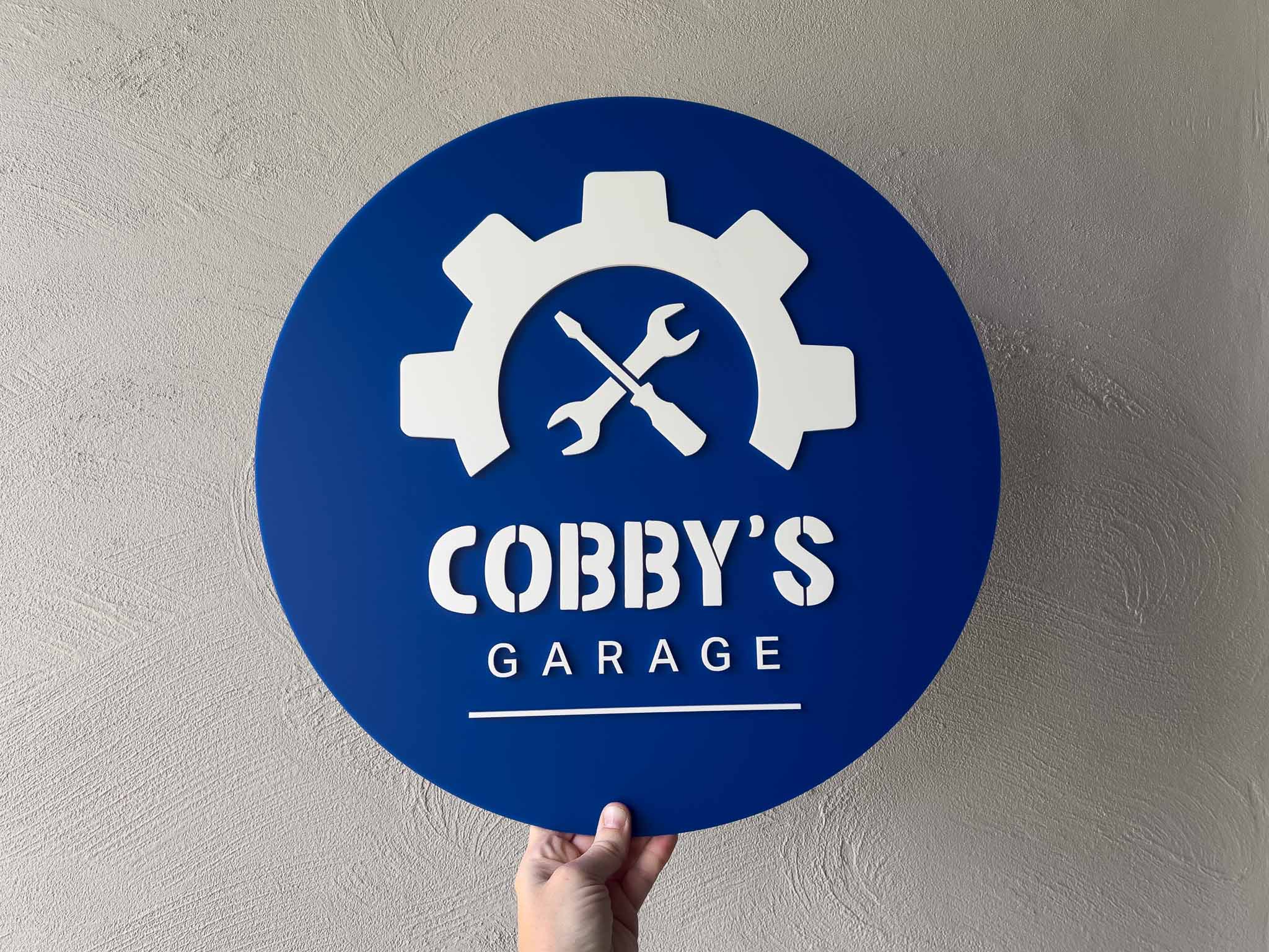 Personalised blue and white mechanic shop style sign that says 'Cobby's Garage'.