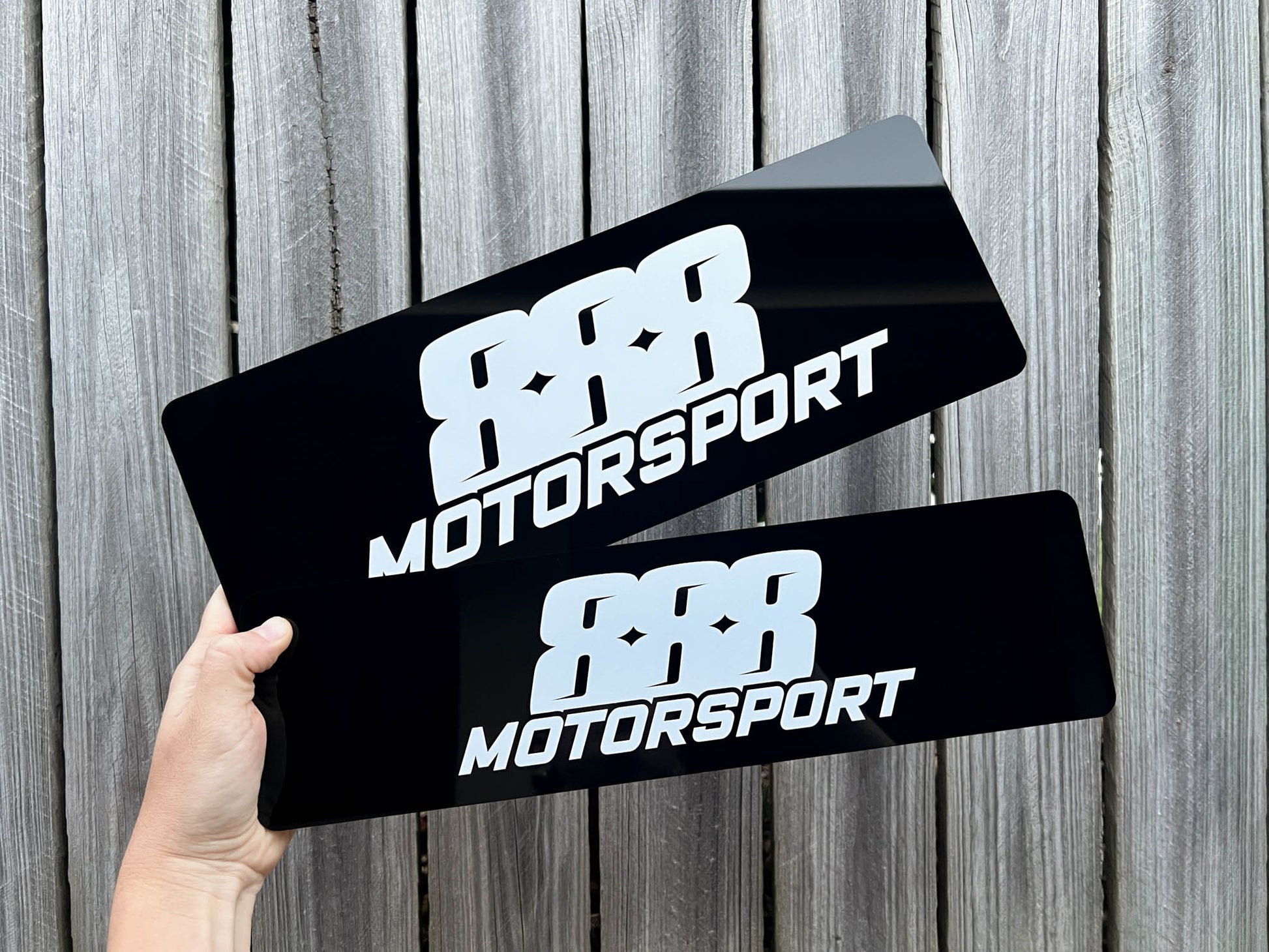 Two black '88R Motorsport' acrylic logo plates held against a wooden background