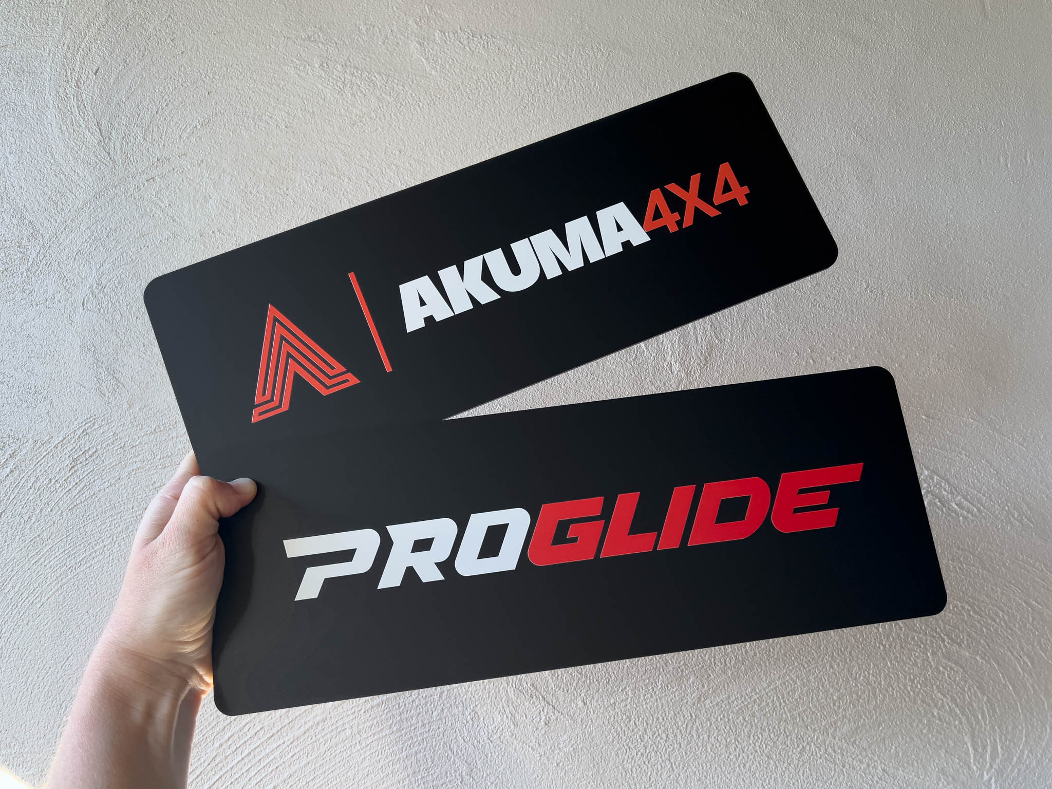 Two black logo cover plates with 'Akuma 4x4' and 'ProGlide' branding held by a hand against a light background.