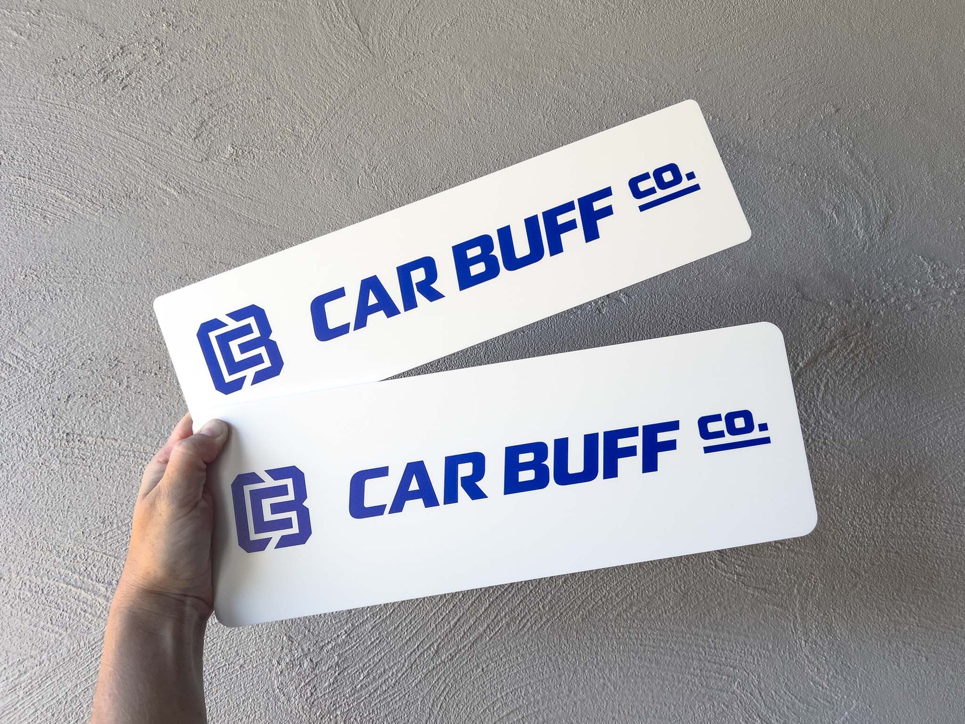Two 'CAR BUFF CO.' logo cover plates held by a hand on a grey background