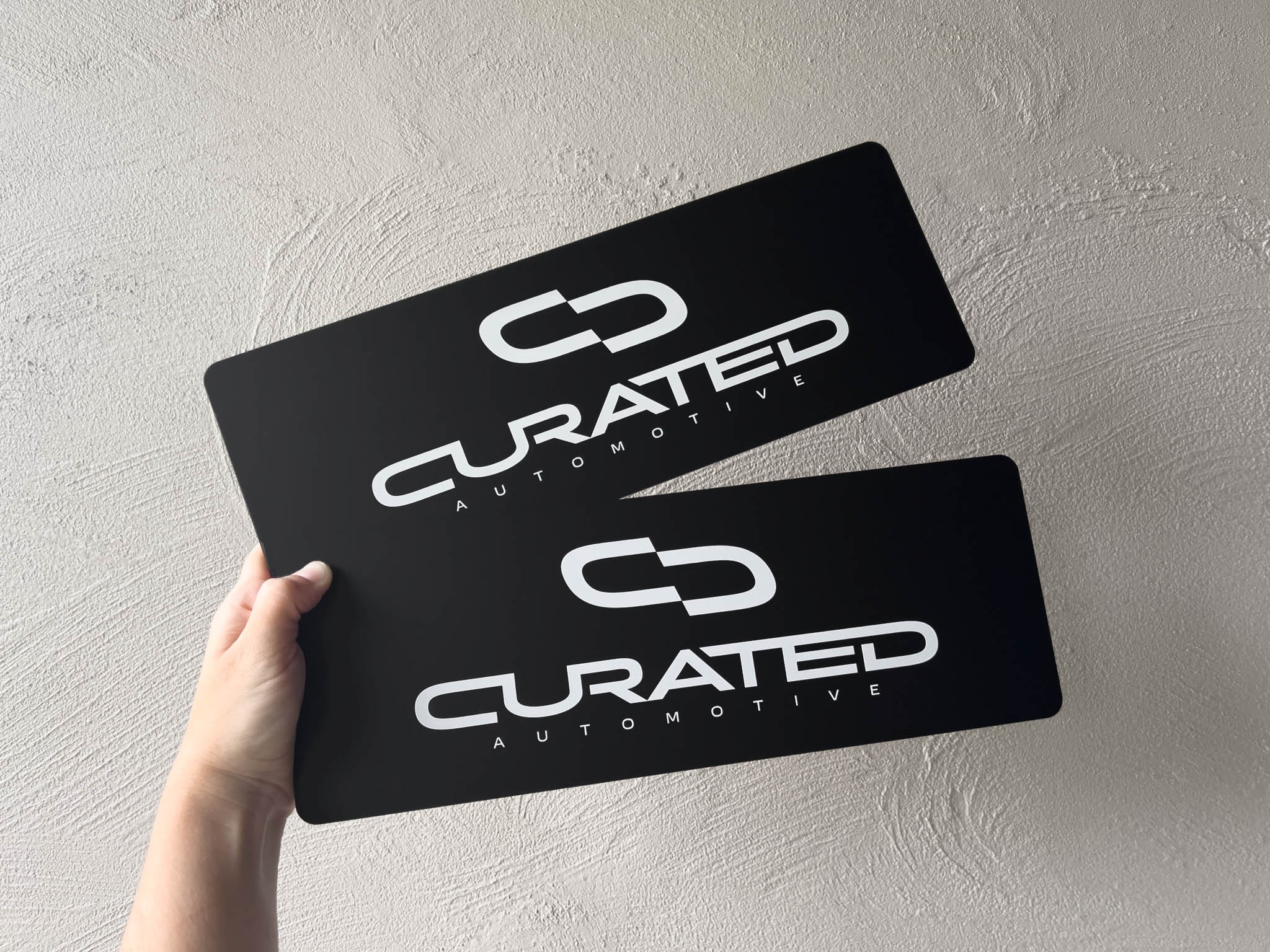 Two black personalised  'Curated Automotive' logo plates printed with UV ink in a matte finish.