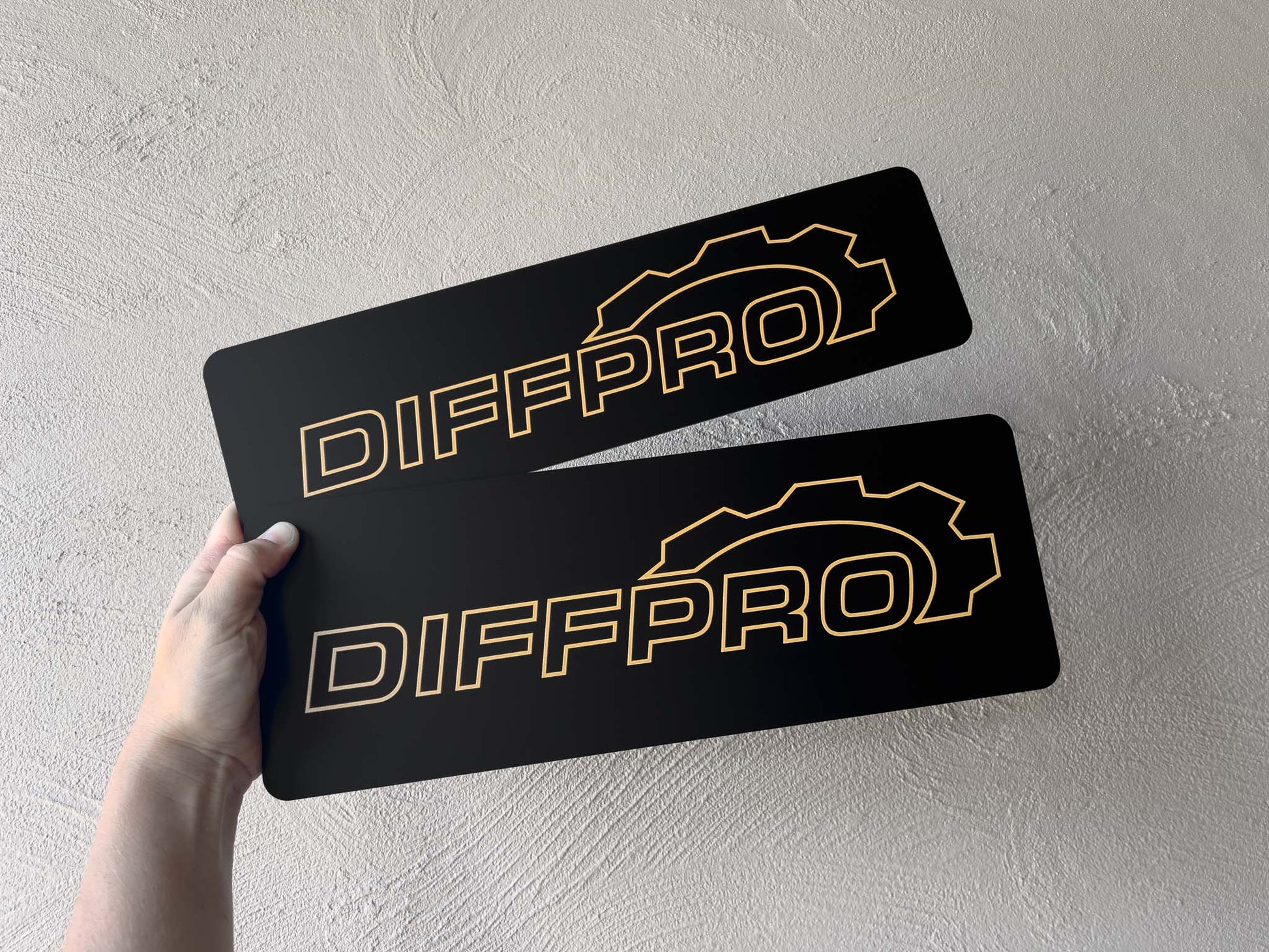 Two black UV printed logo cover plates with 'DIFFPRO' logo held by a hand against a light grey background