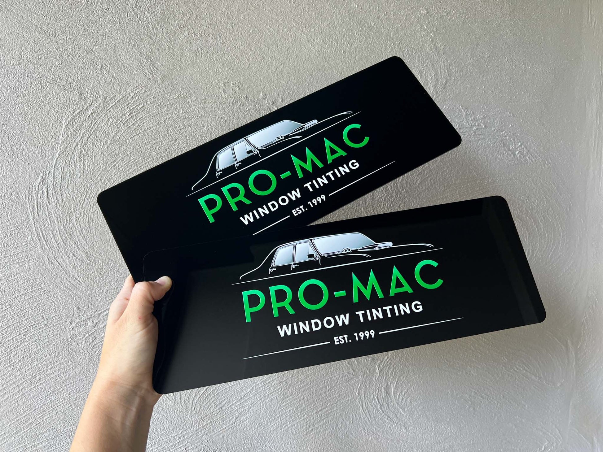 Two black logo cover plates with 'Pro-Mac Window Tinting' branding held by a hand.