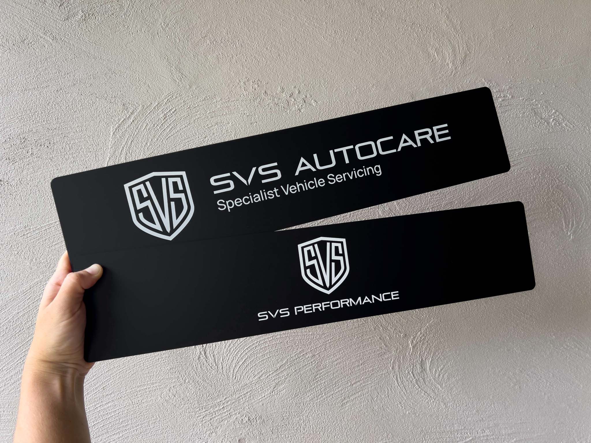 Two black logo plates with 'SVS Autocare' and 'SVS Performance' text held against a light grey background.