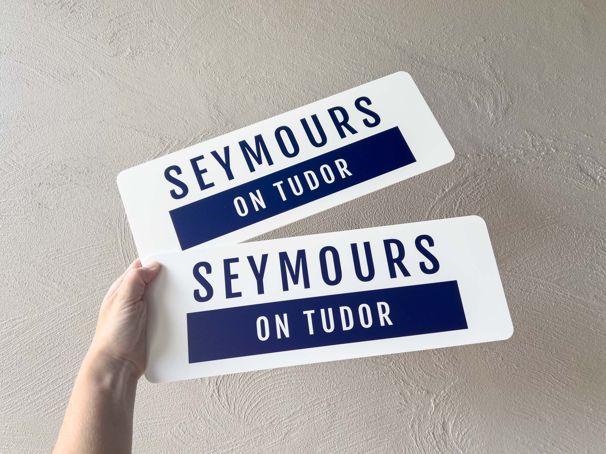 Two custom printed logo plates with 'SEYMOURS ON TUDOR' text held against a light grey background.