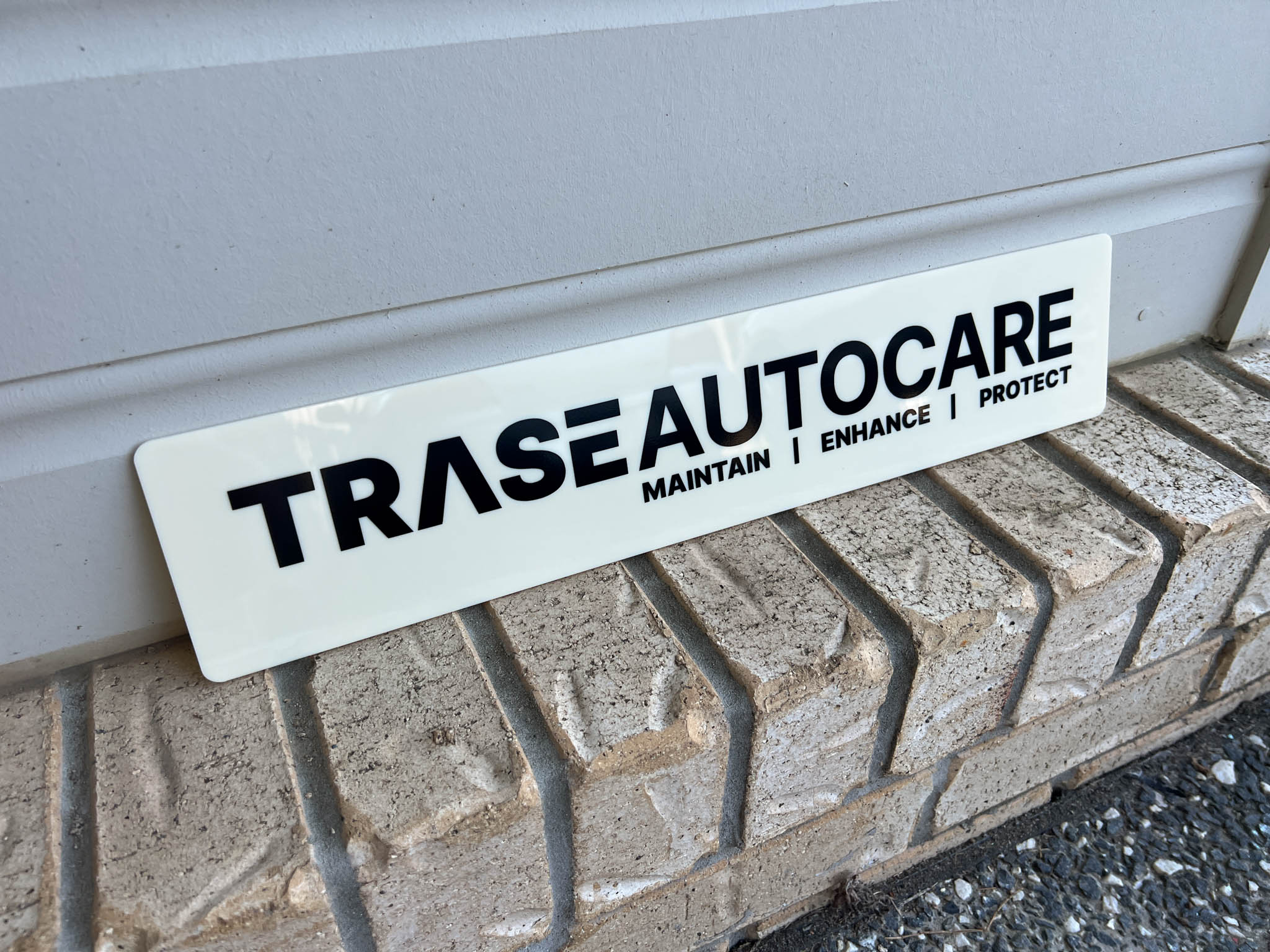 TRASE Autocare Euro logo plate UV printed in beige and black sitting on a brick ledge.