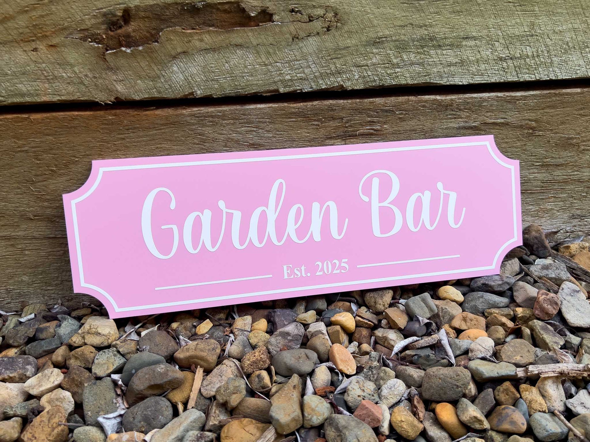 Pink UV printed acrylic sign with 'Garden Bar Est. 2023' printed in white on a wooden background