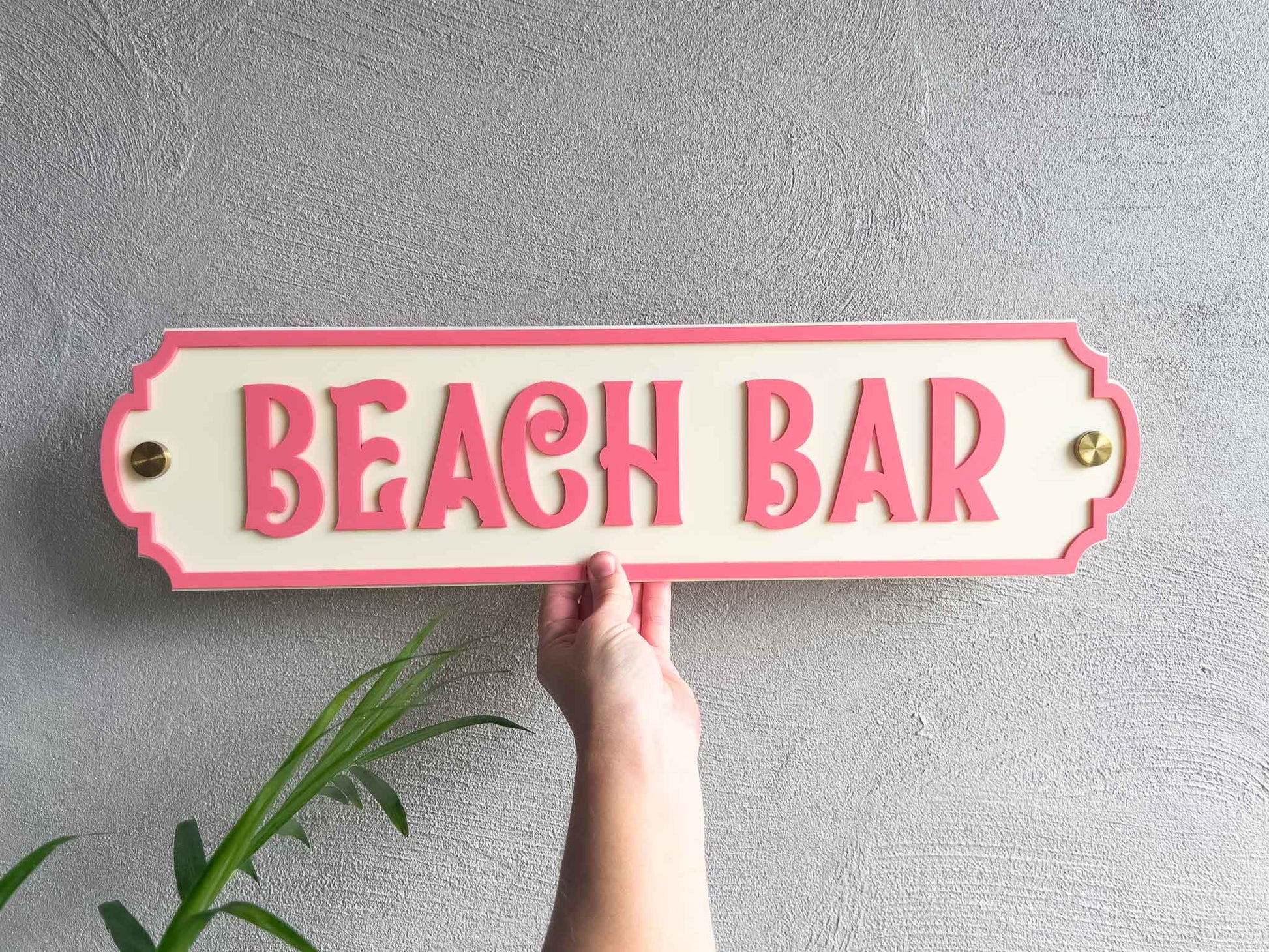 Tropical coral pink and cream beach house sign that reads 'Beach Bar' with gold wall mounts.