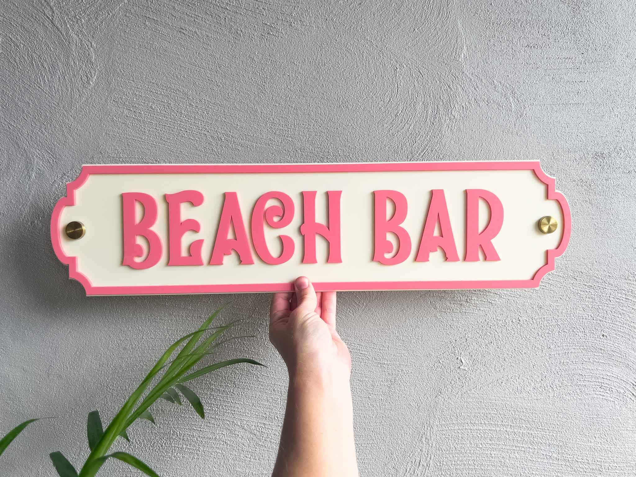 Tropical coral pink and cream beach house sign that reads 'Beach Bar' with gold wall mounts.