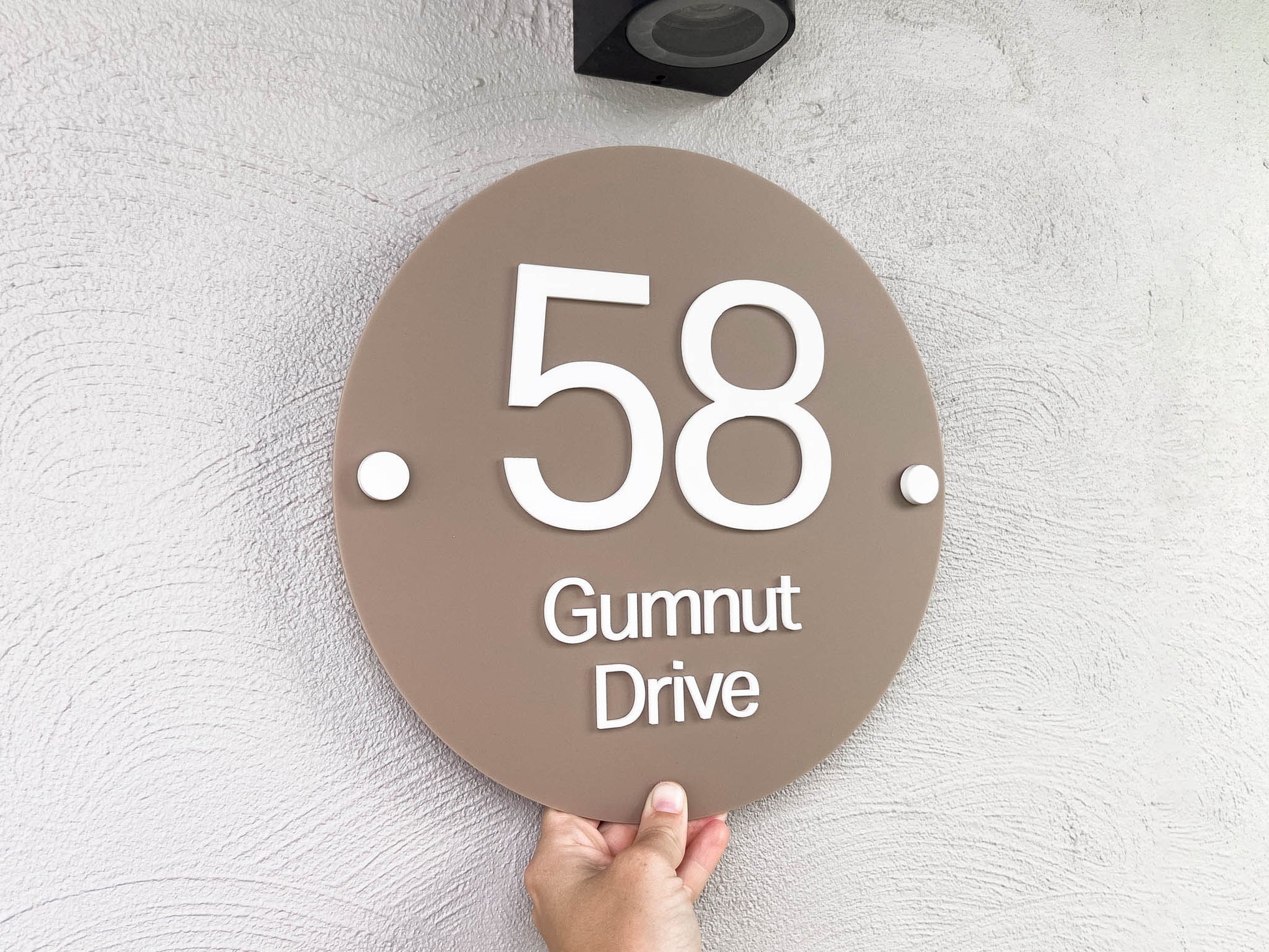 An elegant modern 3D laser cut address sign with the address '58 Gumnut Drive' in white 3D lettering placed on a coconut brown round sign.