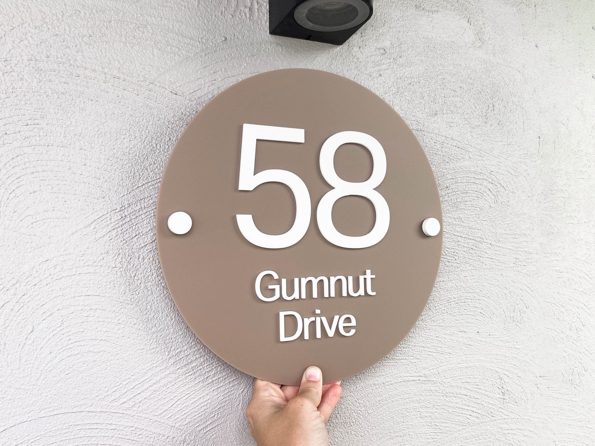 An elegant modern 3D laser cut address sign with the address '58 Gumnut Drive' in white 3D lettering placed on a coconut brown round sign.