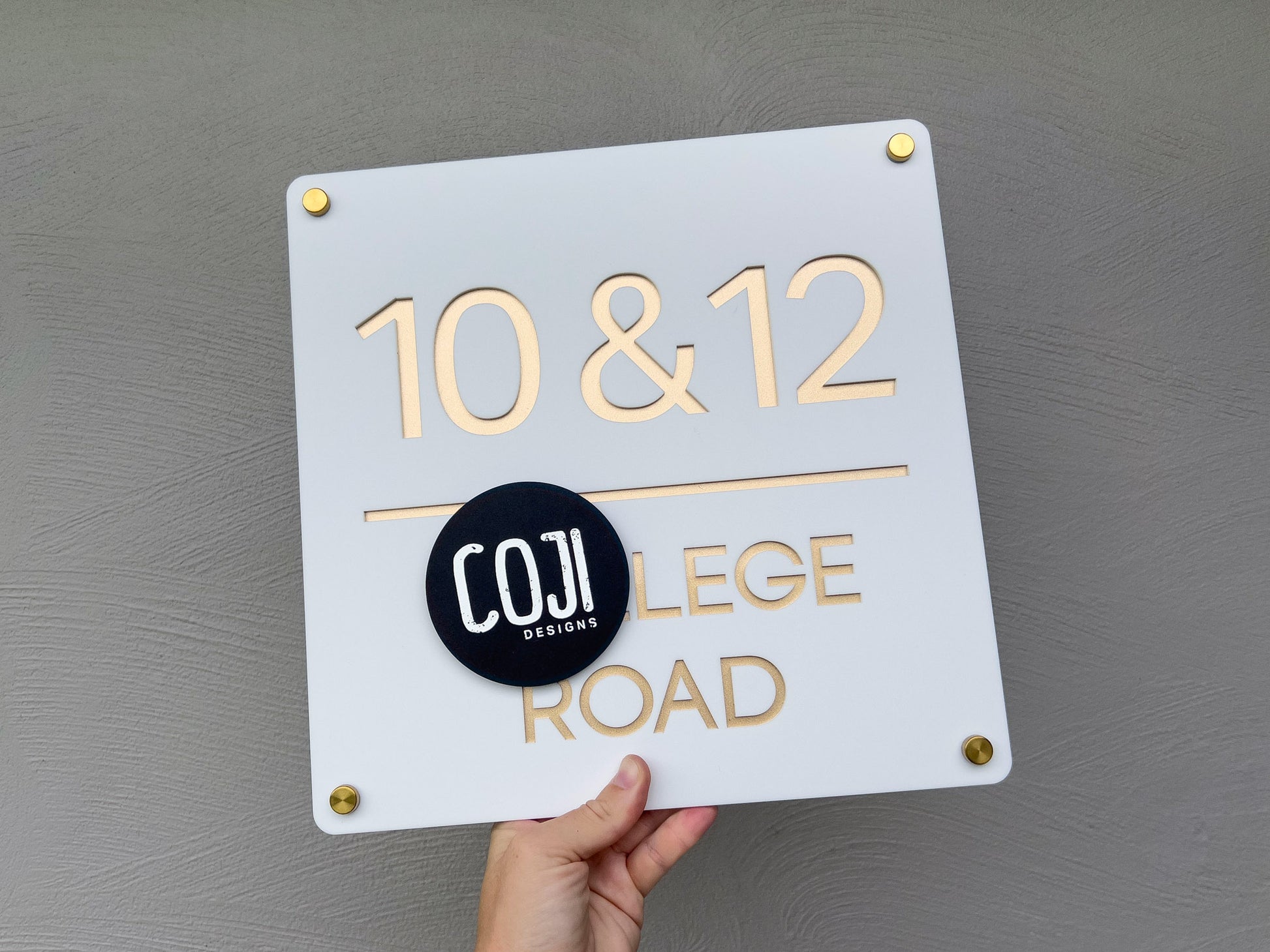 Custom made 3D acrylic laser cut address sign in white and metallic gold that reads the numbers '10 & 12'.