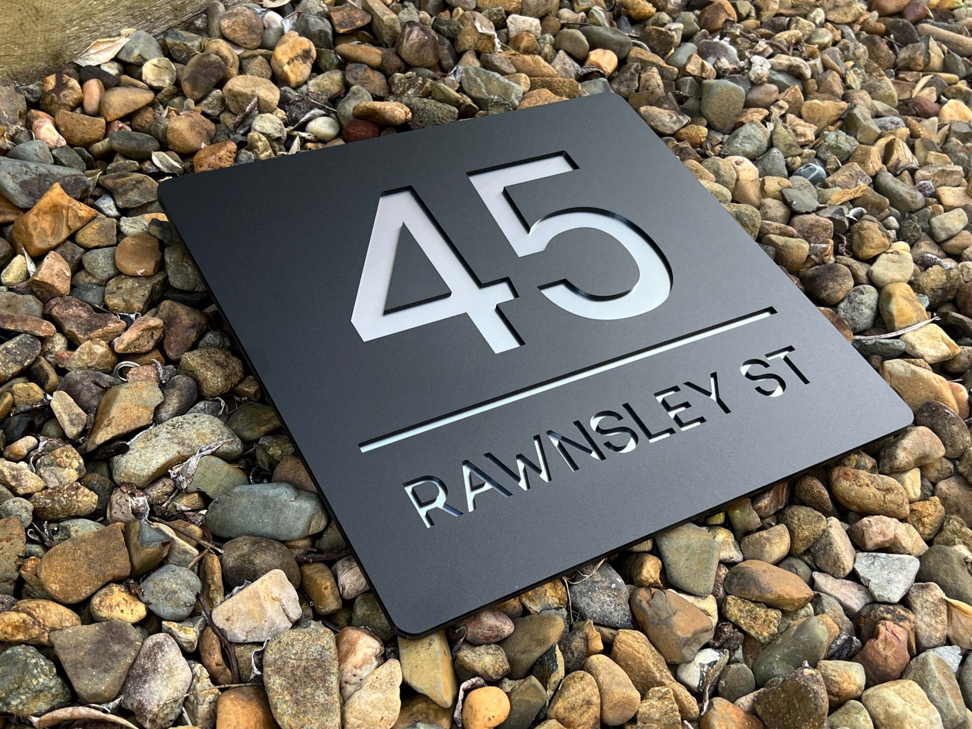 Metallic house number sign with street name on pebbles