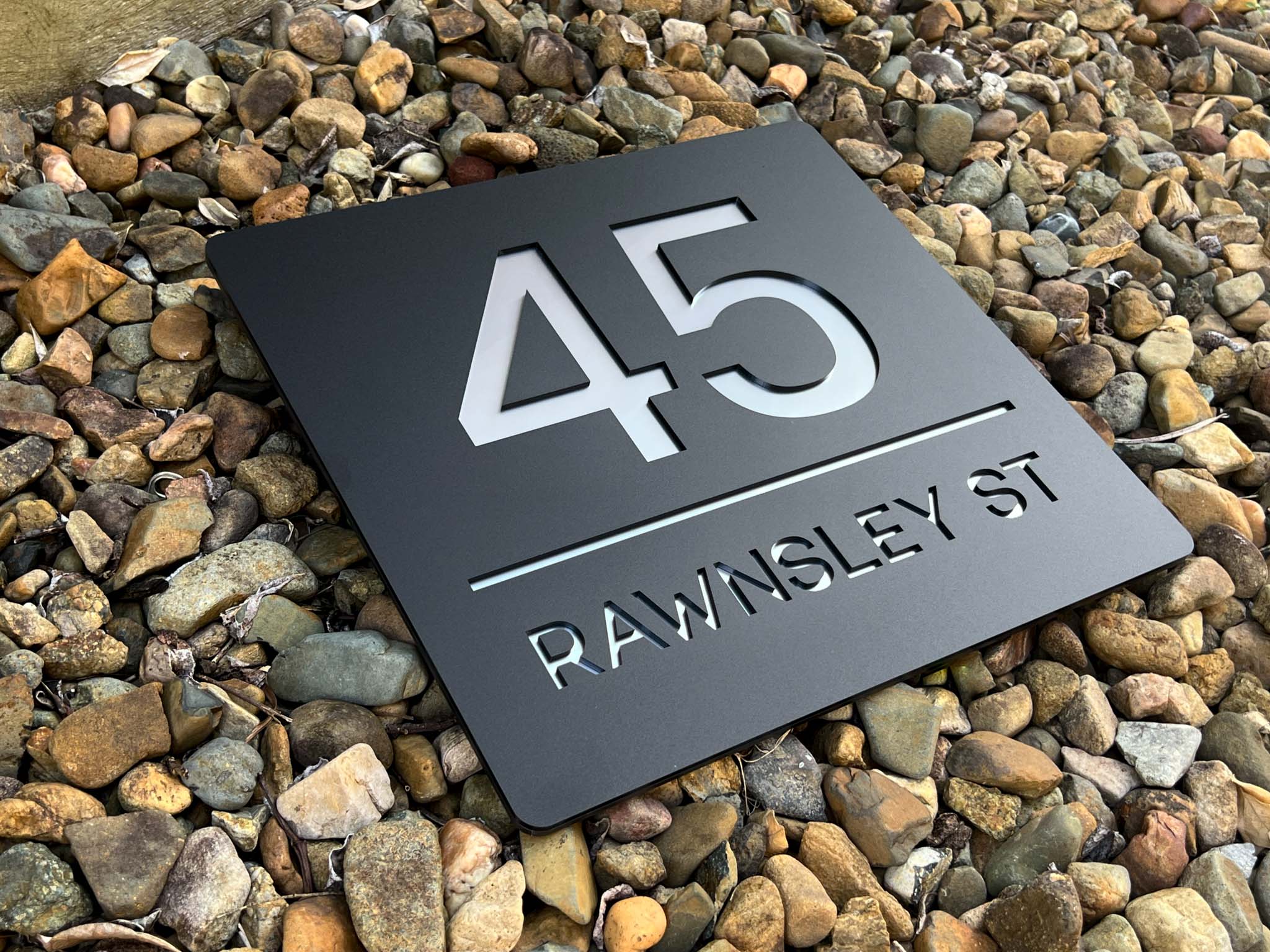 Metallic house number sign with street name on pebbles