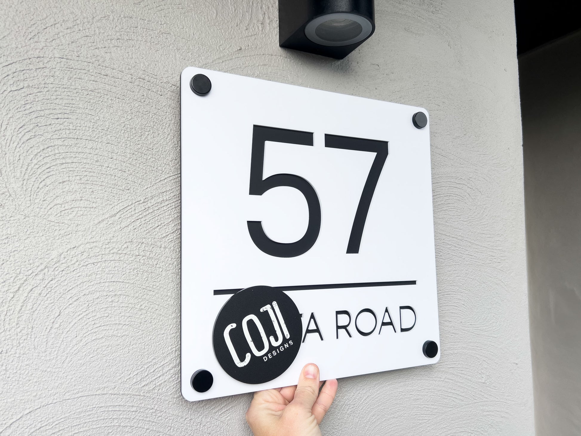 Modern black and white 3D laser cut acrylic home address sign that reads '57 Road' mounted to a wall