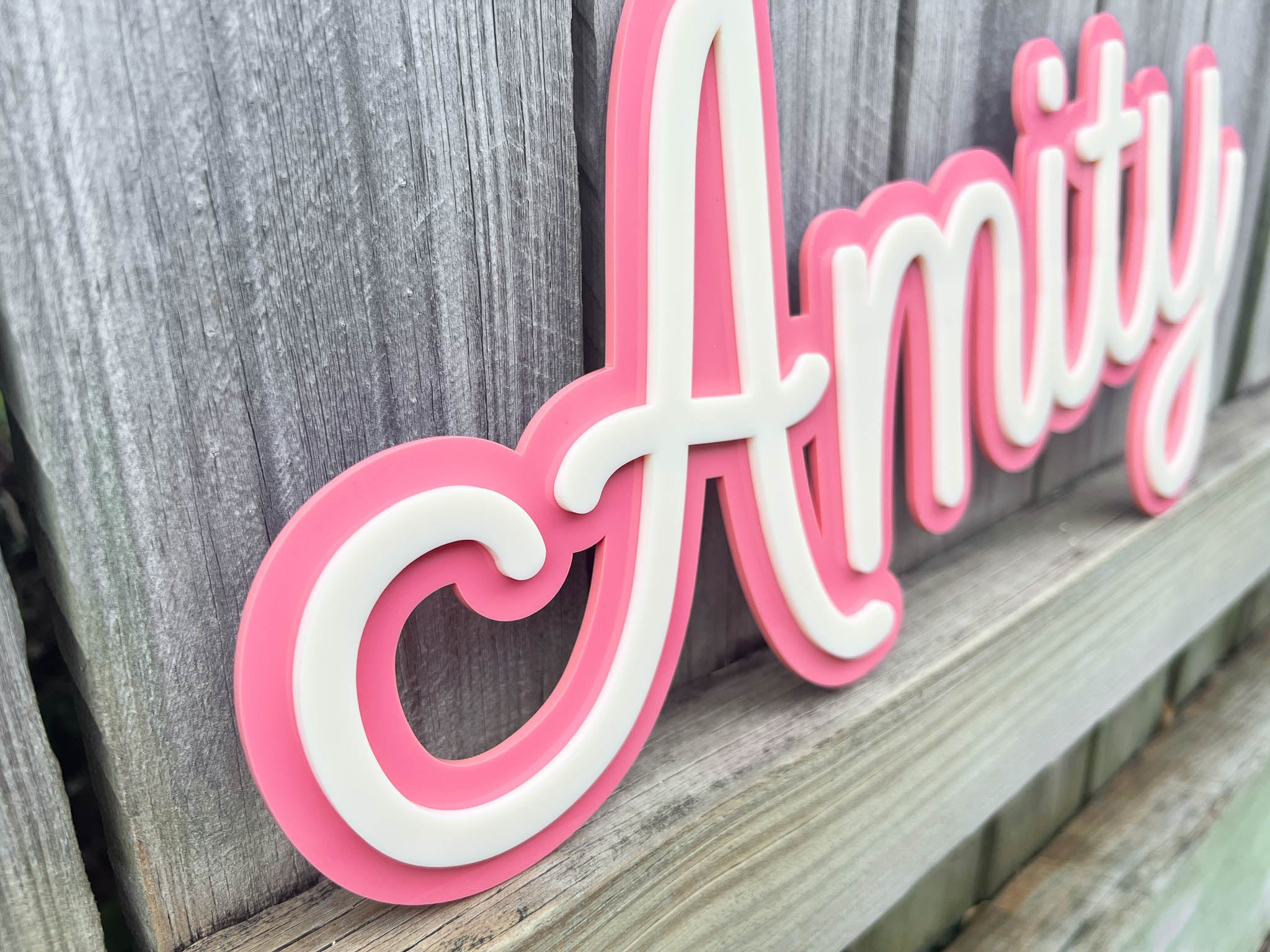 Pink and white decorative sign with 'Amity' on a wooden surface