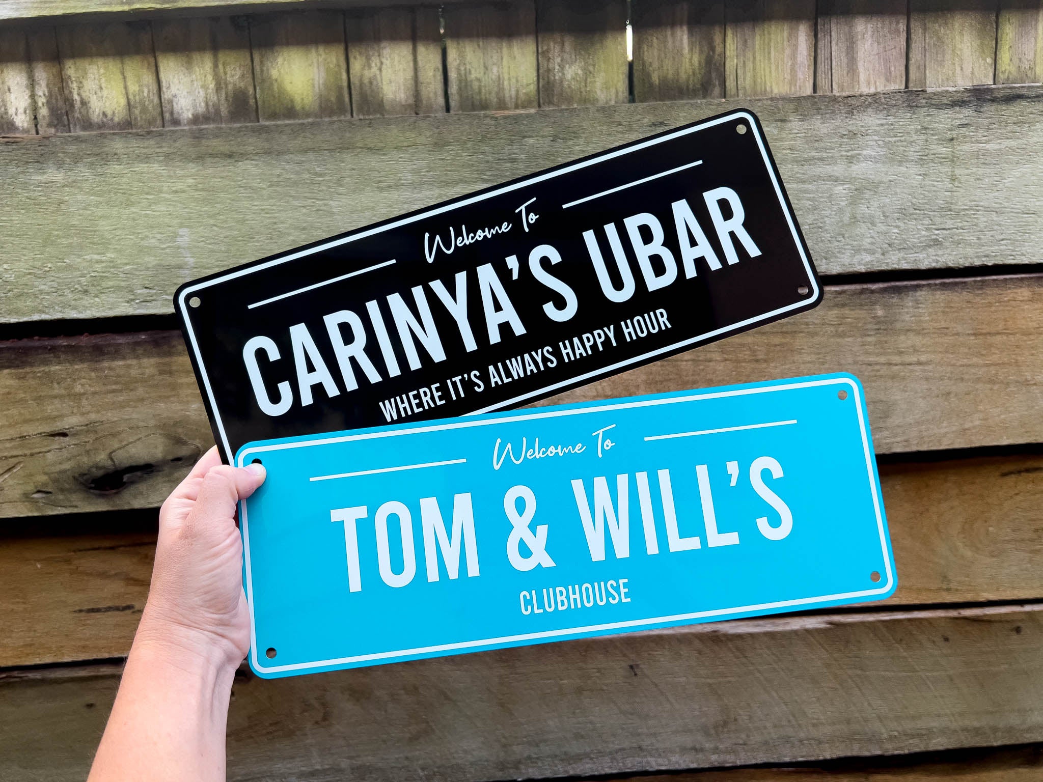 A black and white bar sign that says 'Carinya's Ubar' & a blue and white sign that says 'Tom & Will's Clubhouse'.