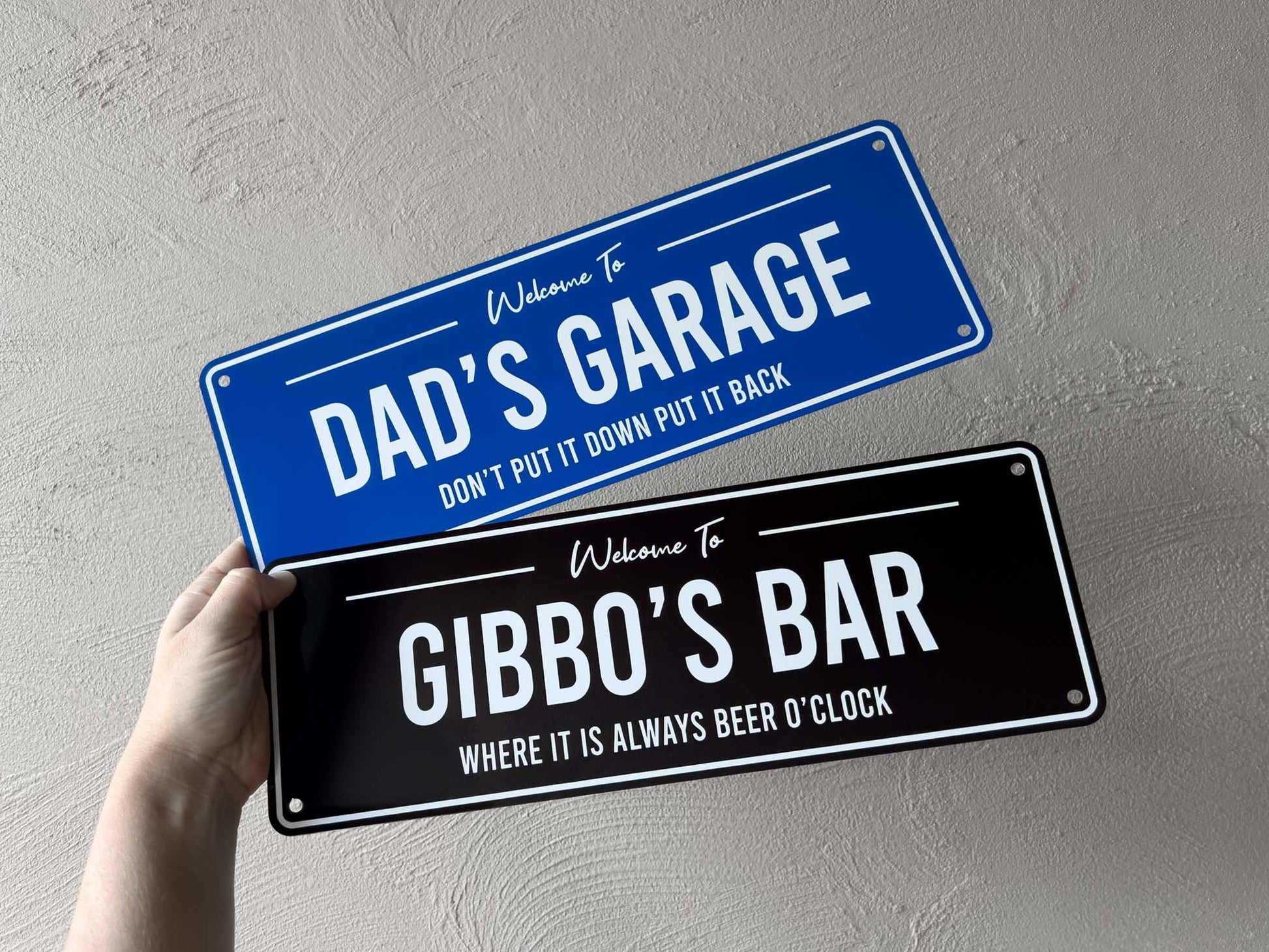Two novelty signs, one for 'Dad's Garage' and one for 'Gibbo's Bar', held against a grey background.