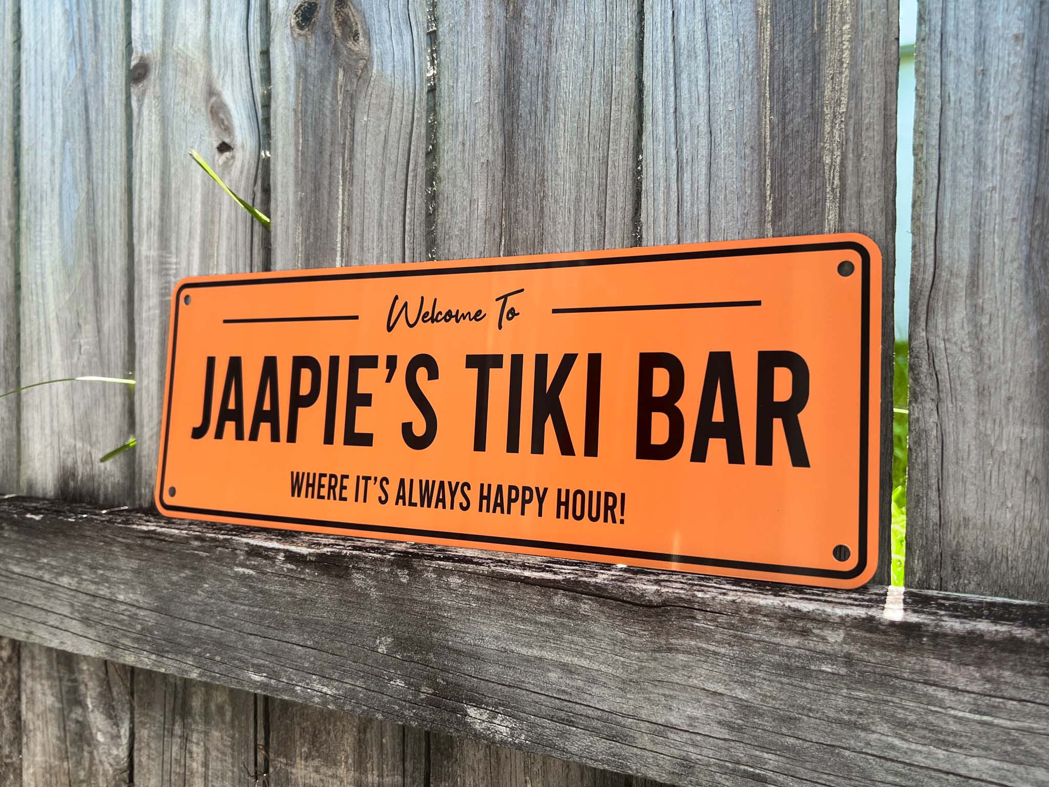 Orange sign with black text reading 'Welcome to Jaapie's Tiki Bar' on a wooden background
