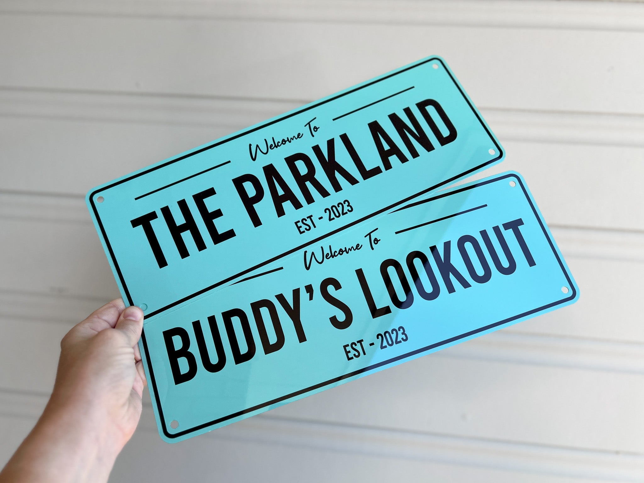 Two minty blue coloured metal plates with black text that says 'The Parkland' & 'Buddy's Lookout'.