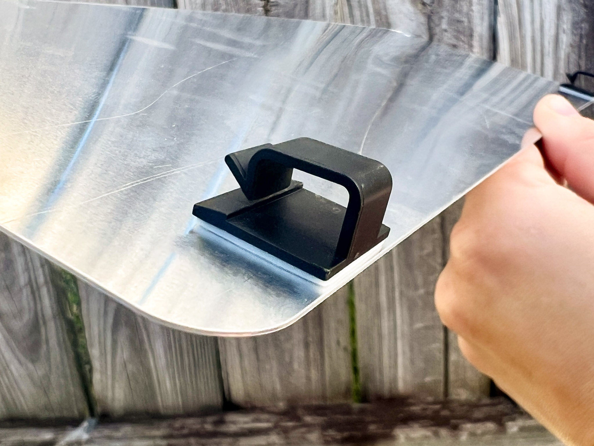 Hand holding an aluminium logo plate with two black plastic mounting clips.