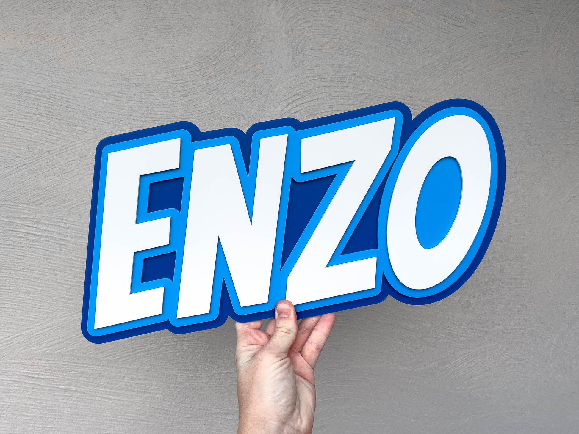 Retro high impact text name plaque in blue and white that reads 'ENZO'.