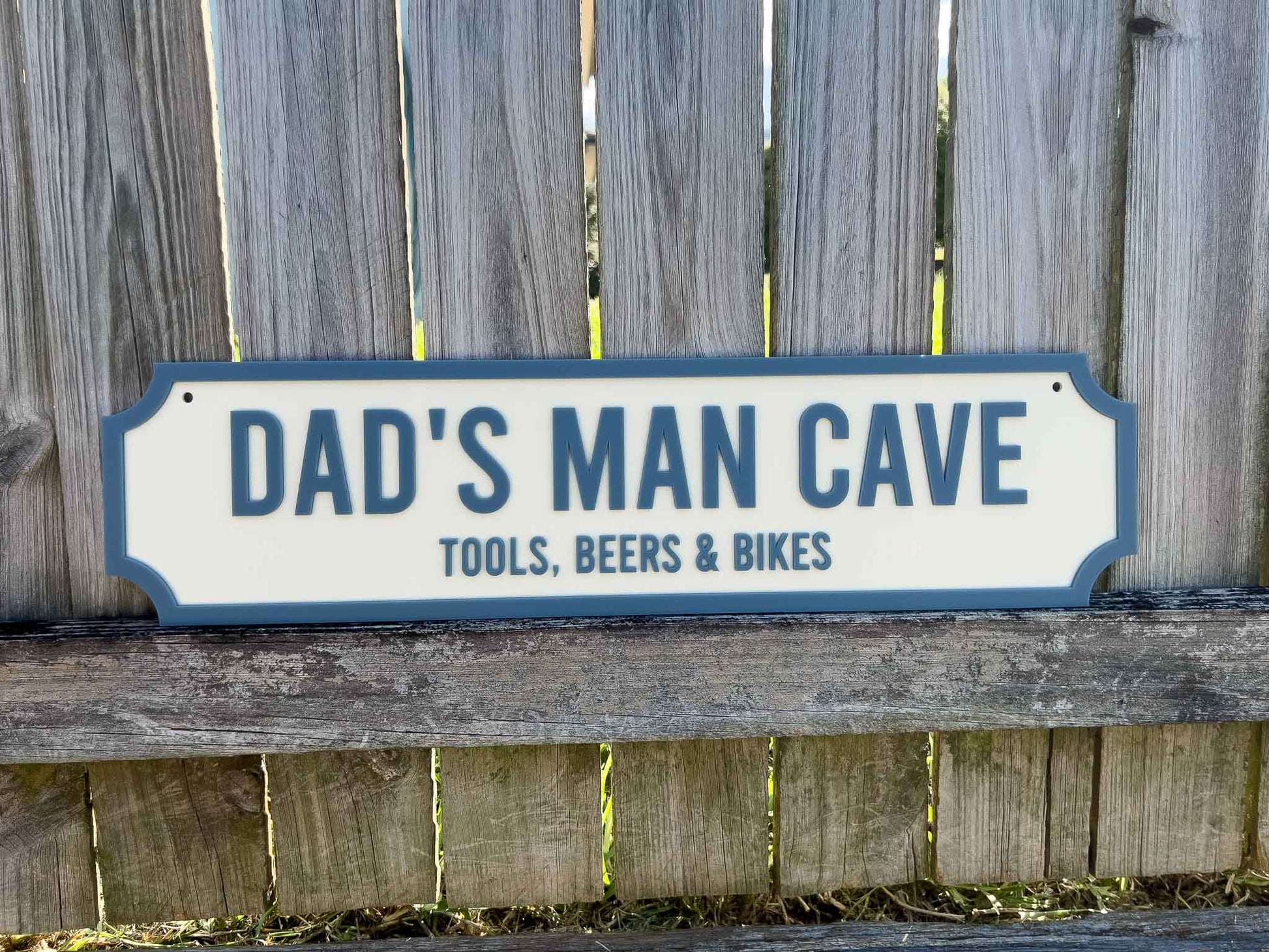 Decorative sign reading 'Dad's Man Cave: Tools, Beers & Bikes' against a wooden fence background.