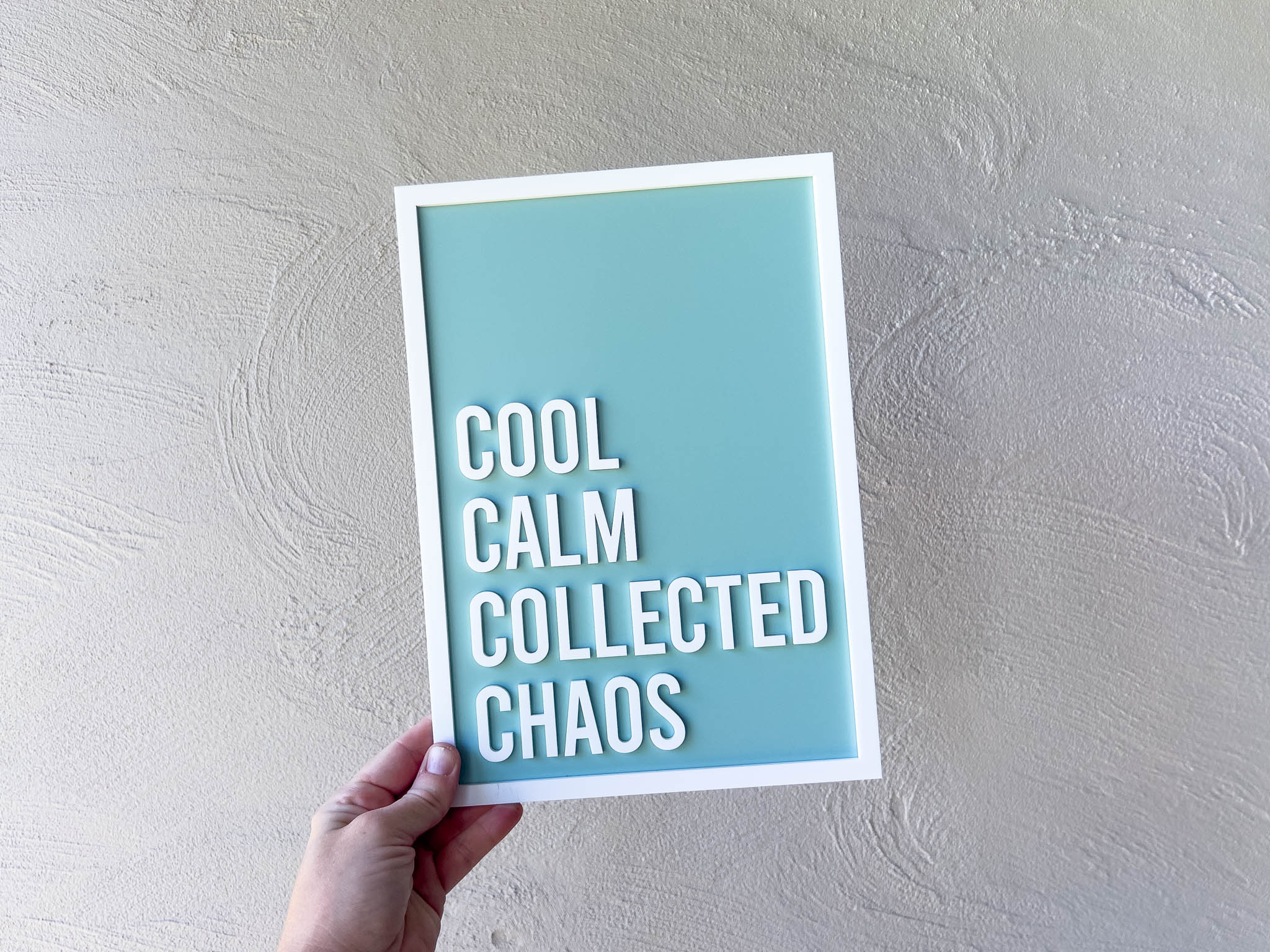 Hand holding a framed 3D acrylic custom made sign with 'Cool Calm Collected Chaos' text against a light grey background.