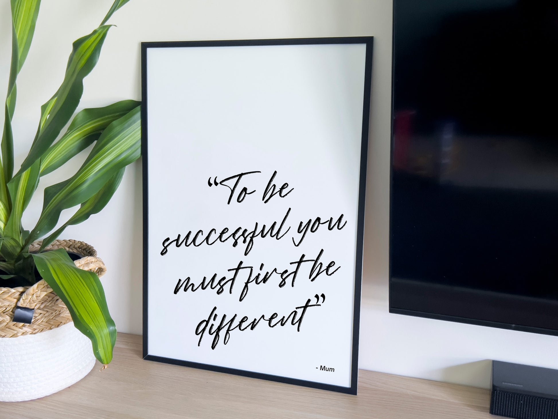 Framed motivational quote on a desk with a plant and computer monitor in the background