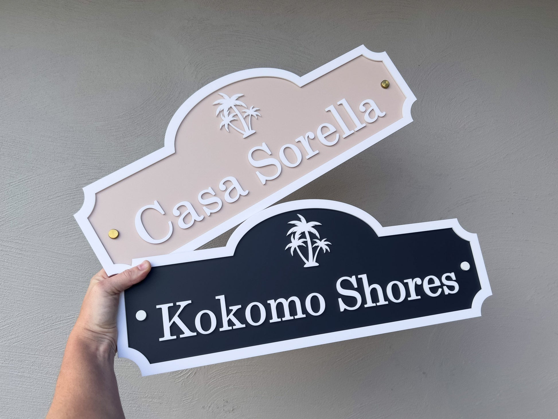 Two decorative signs with 'Casa Sorella' in dark blue and white and 'Kokomo Shores' in beige and white on a plain background.